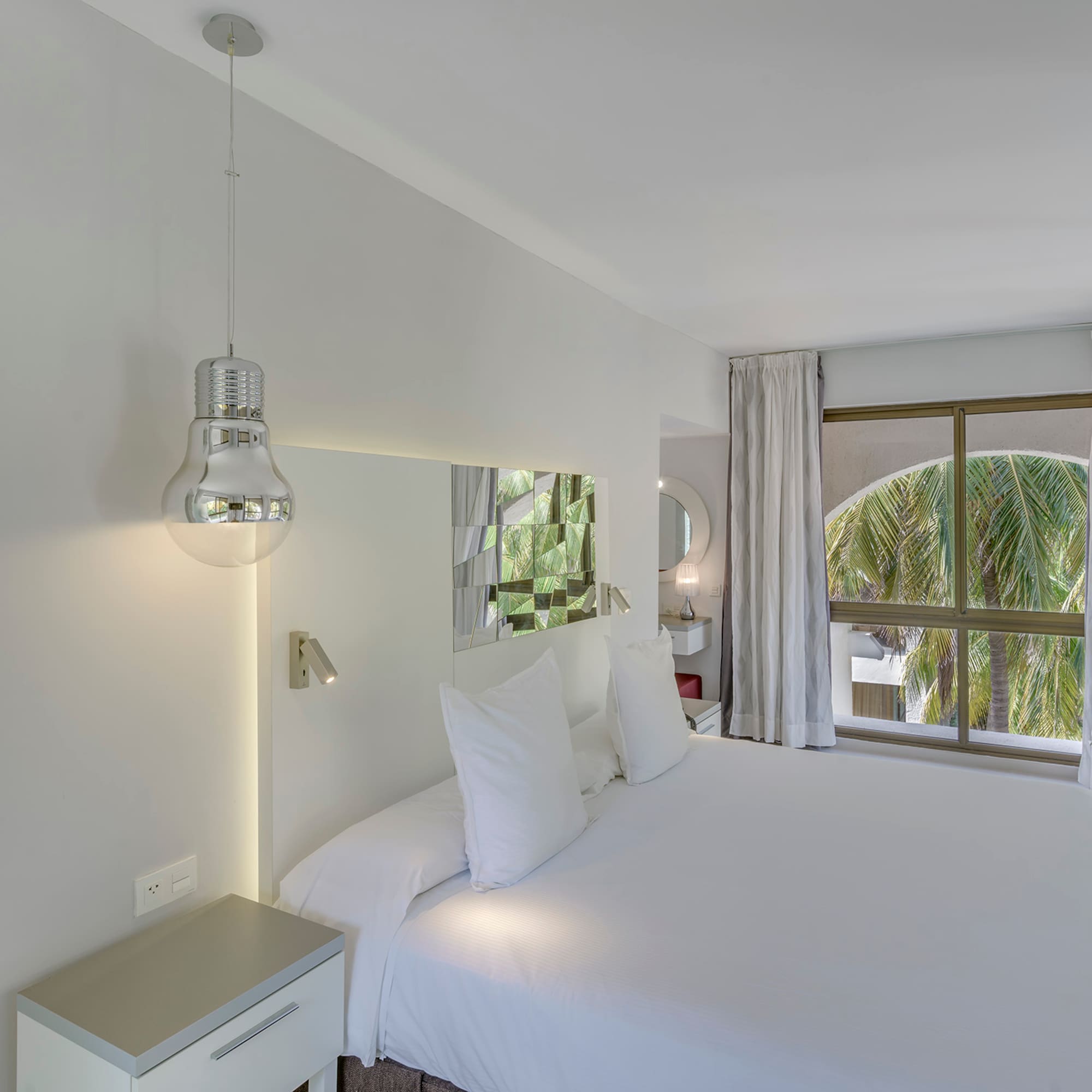 a white bed with white sheets and a mirror above it