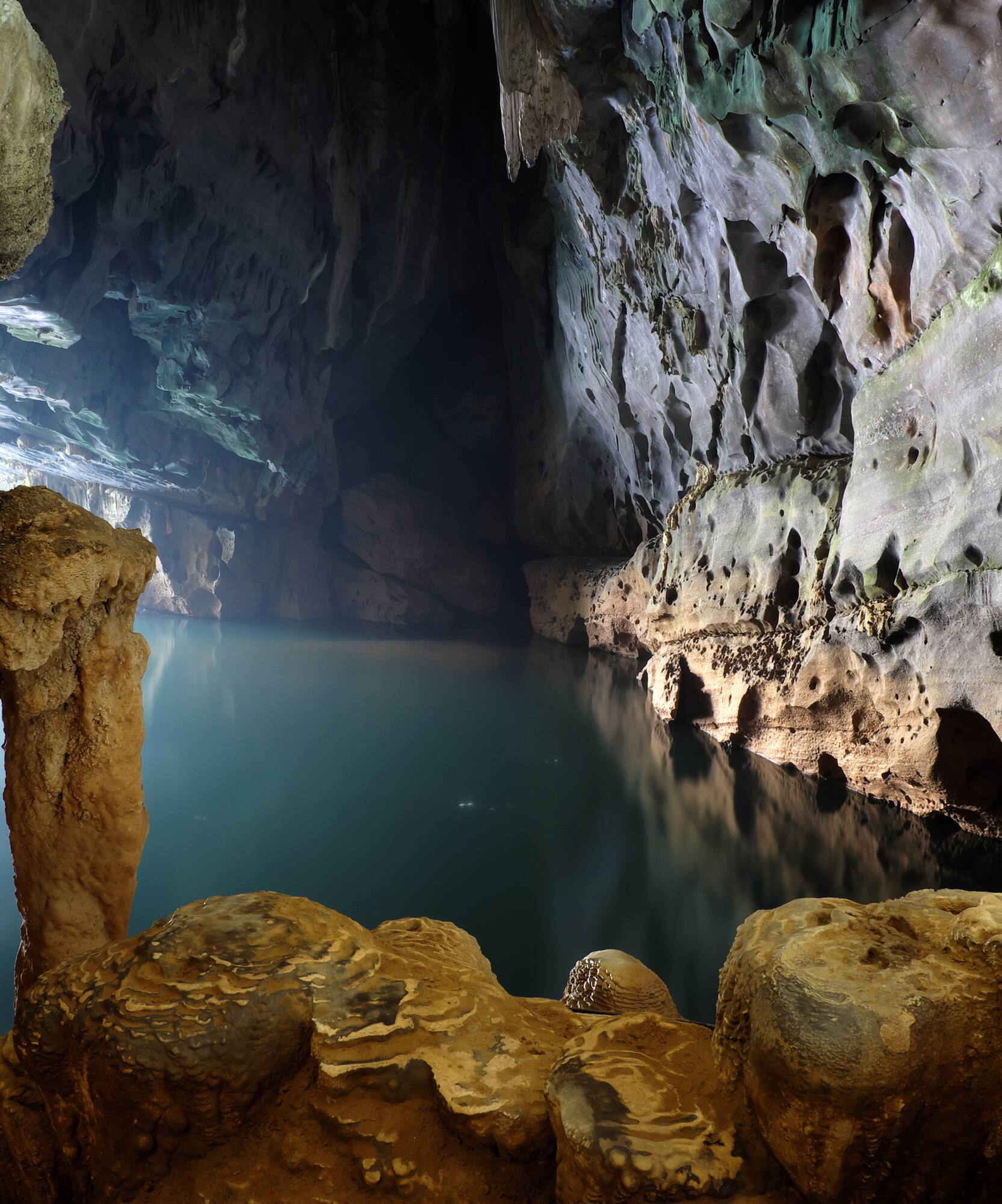 Dark cave with illuminated underground lake and rugged rock formations.