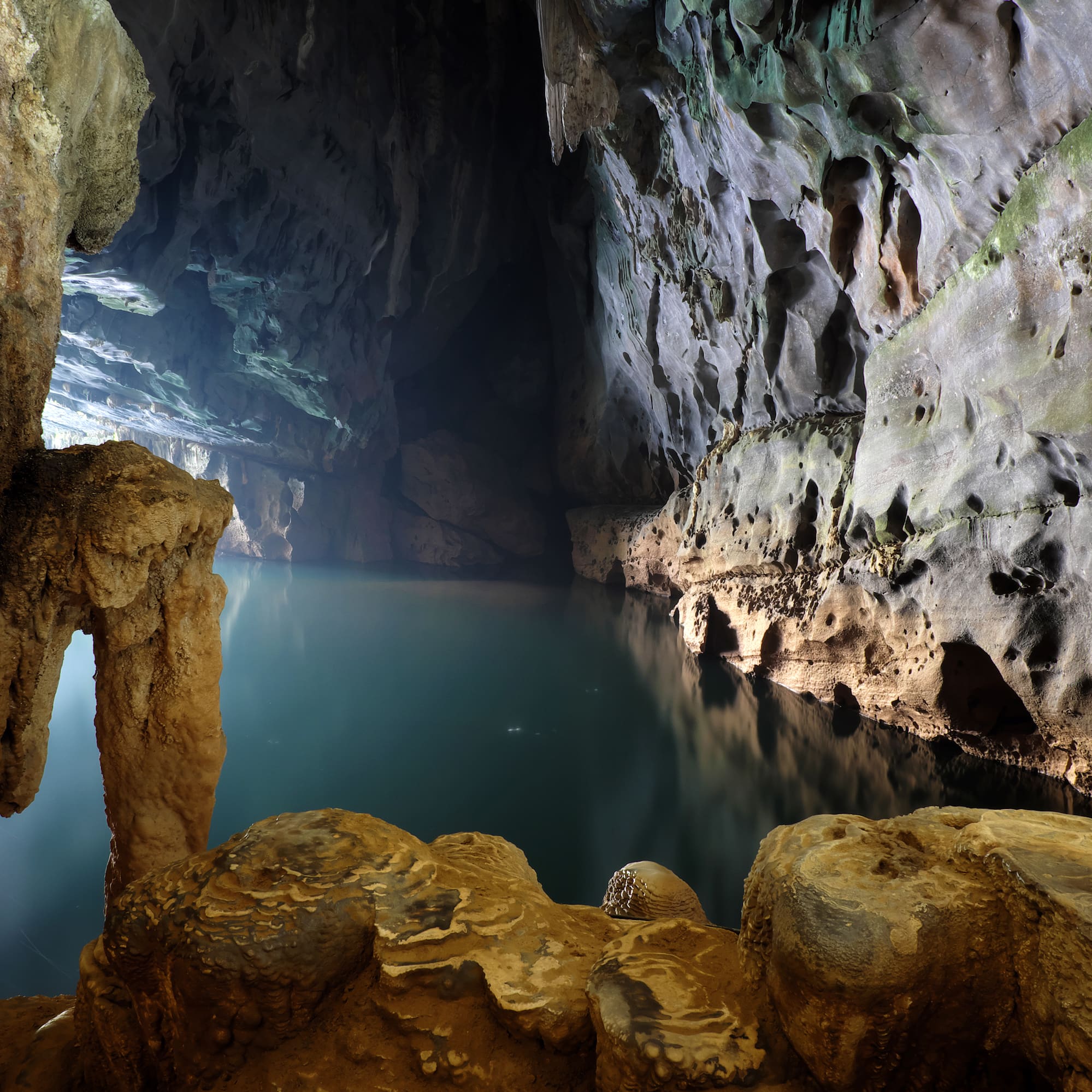 Dark cave with illuminated underground lake and rugged rock formations.