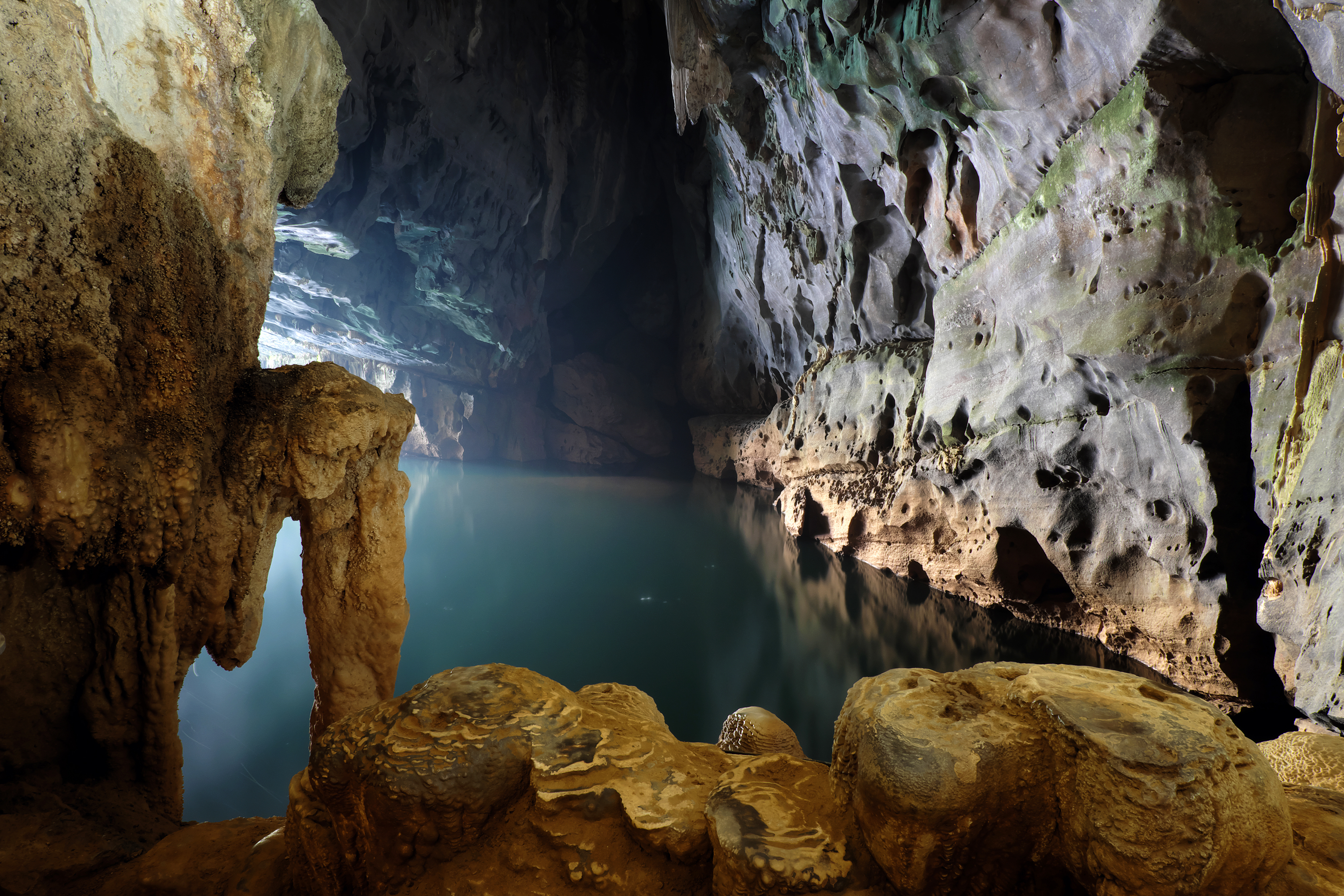 Dark cave with illuminated underground lake and rugged rock formations.