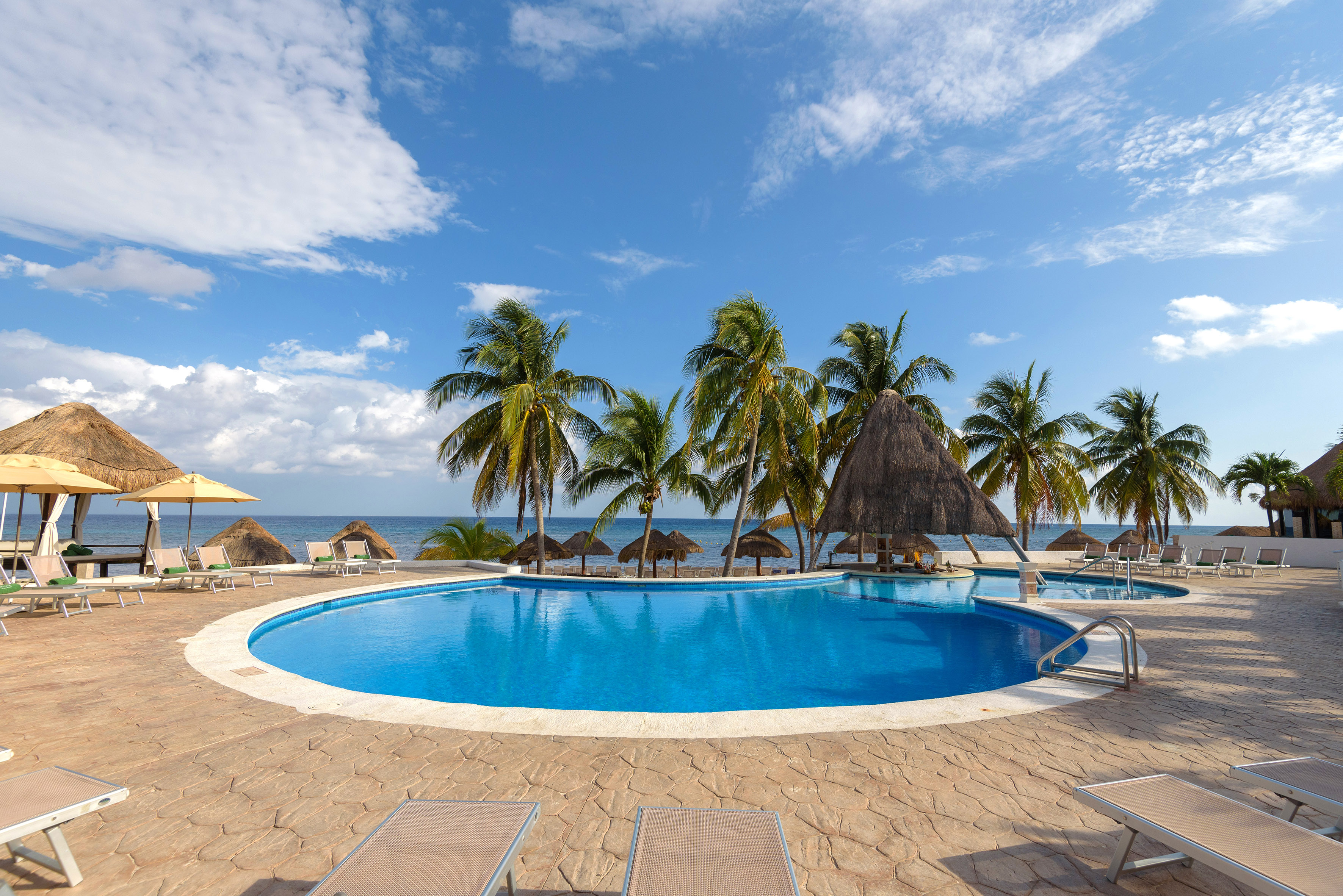a pool with palm trees and umbrellas on the beach