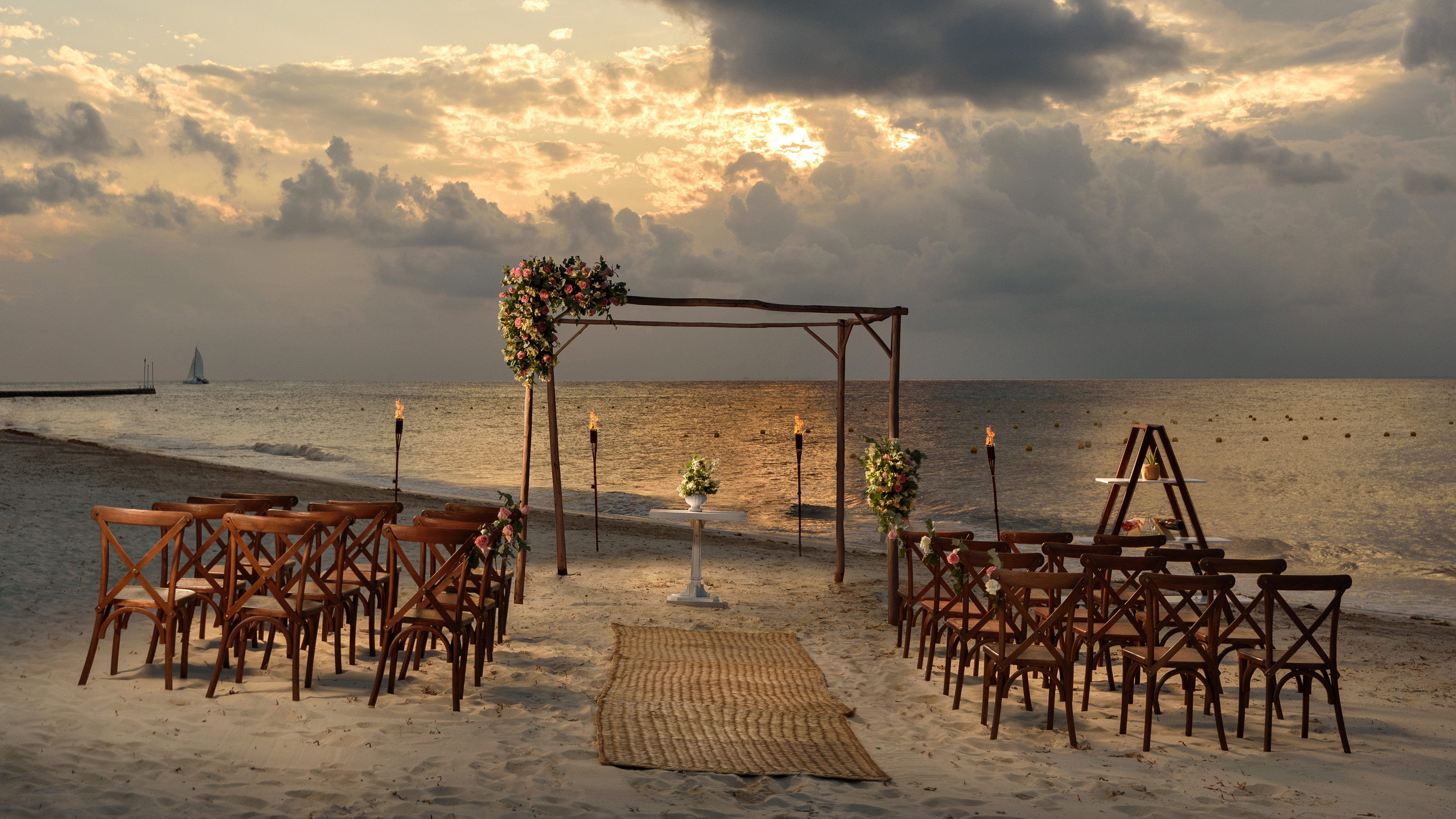 Beach wedding ceremony setup at sunset with floral arch and ocean backdrop.