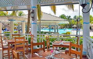 a restaurant with tables and chairs and a pool in the background