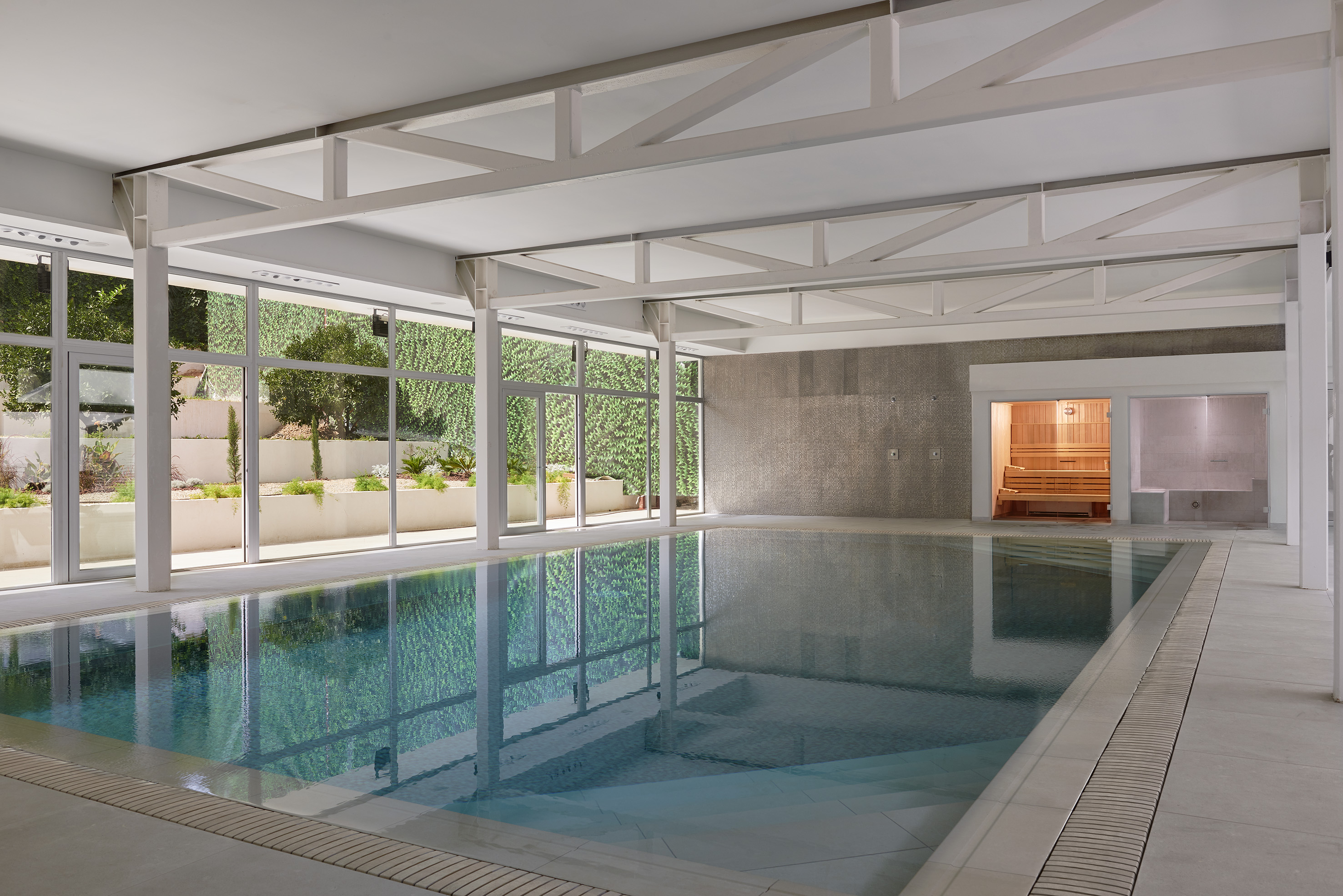 Modern indoor swimming pool with garden view windows and sauna room.