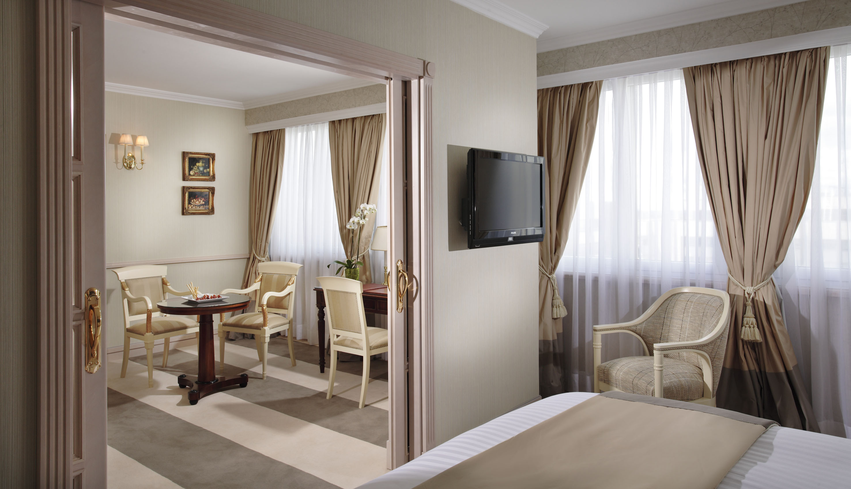 Elegant hotel suite with bedroom, separate dining area, and flat-screen TV.