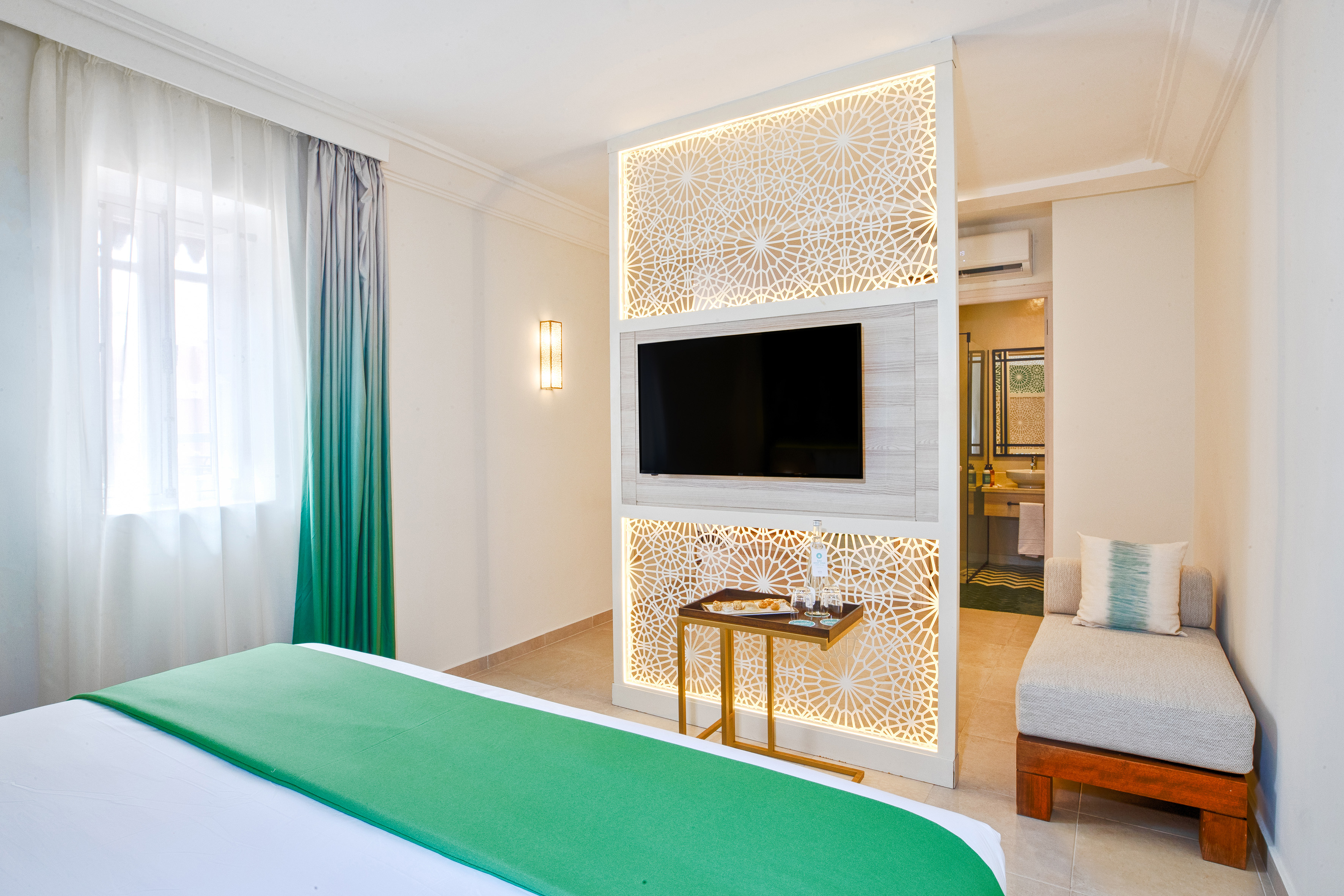 Elegant hotel room with TV, geometric partition, green bed runner, and lounge. - Family Room - SOL Oasis Marrakech, Marrakech