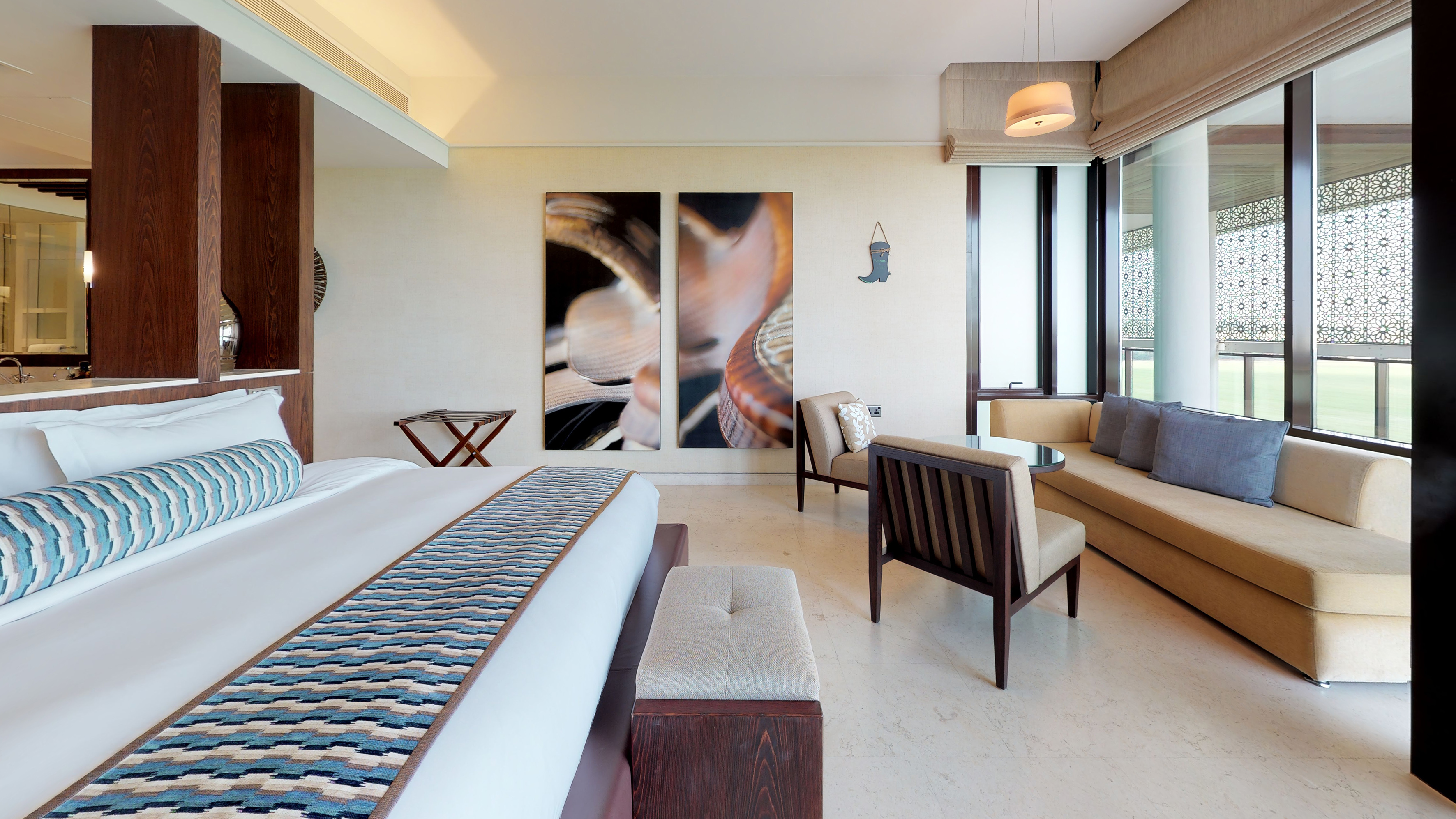 Modern bedroom interior with large bed, patterned runner, beige sofa, and abstract art.