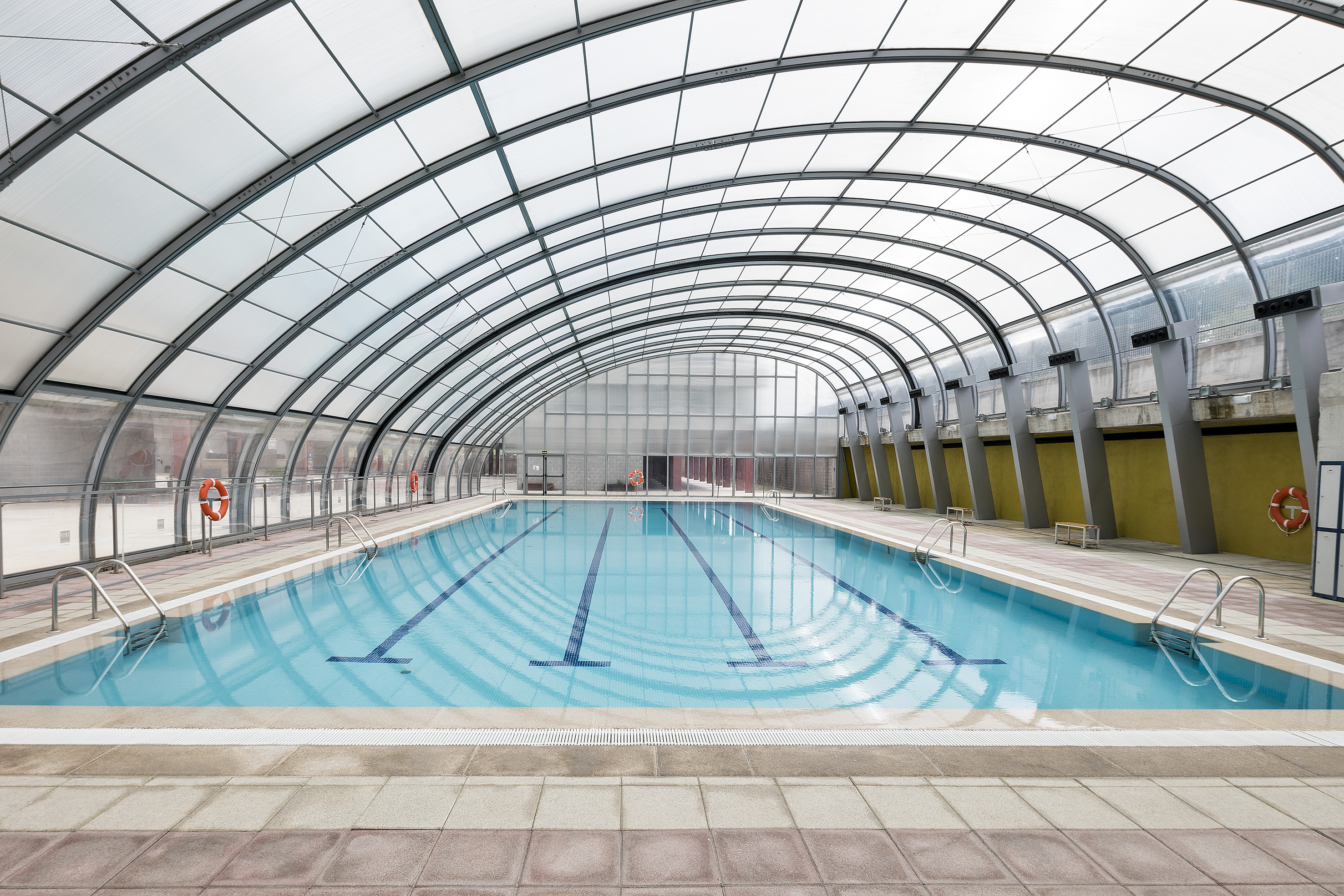 Indoor swimming pool with arched translucent roof, blue water, and lane lines.