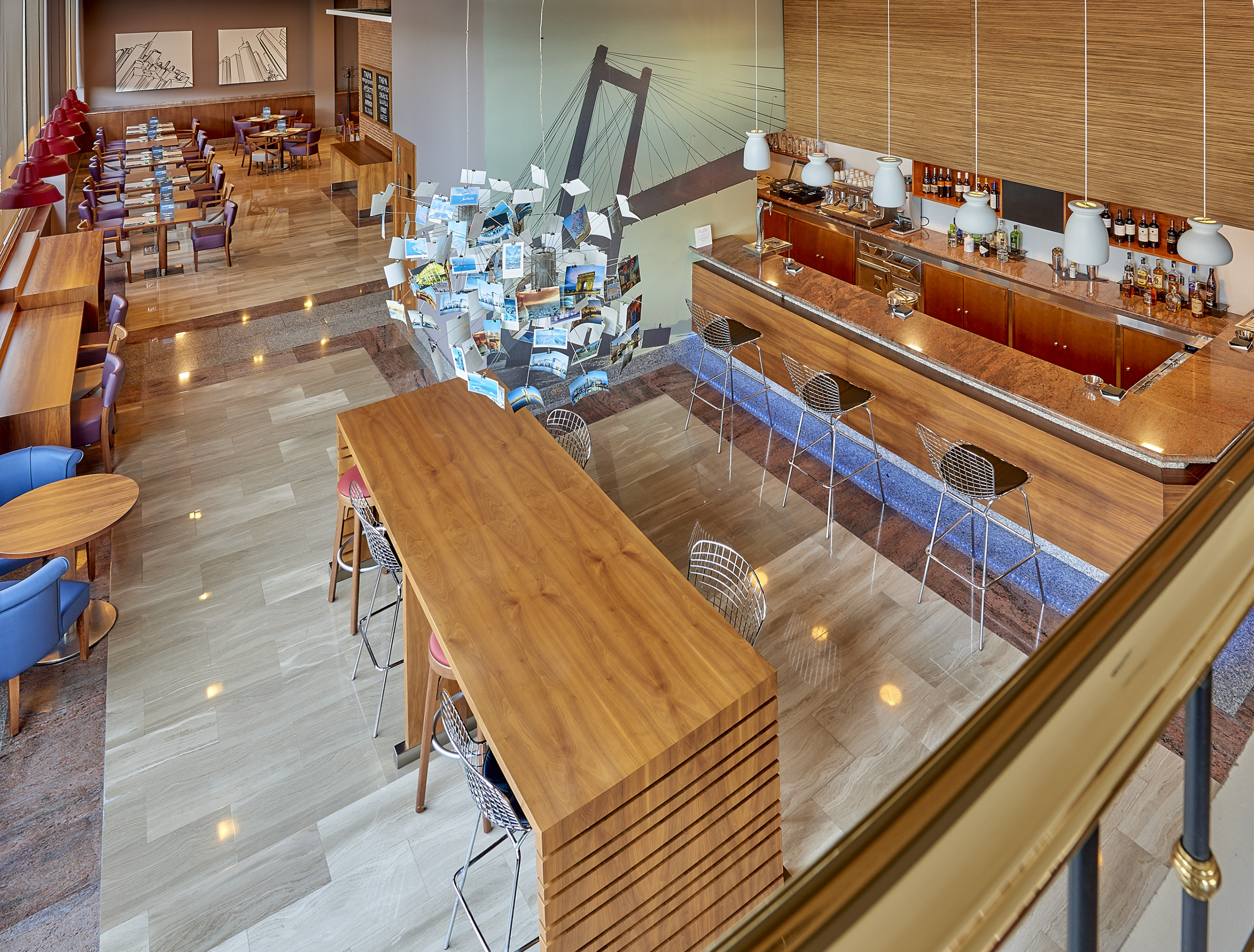 Modern hotel lounge bar with dining, communal table, and postcard artwork.