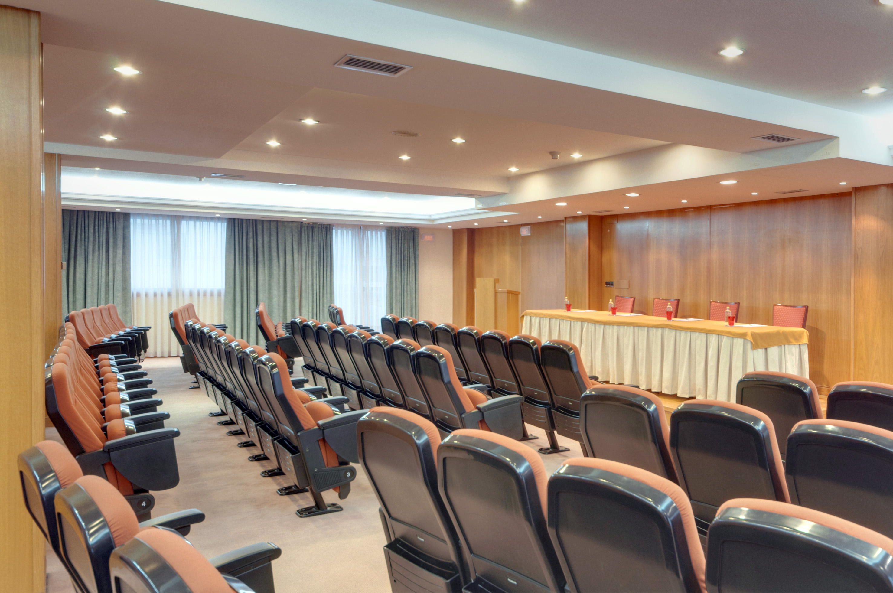 Empty conference room with rows of orange seating and a presentation stage.