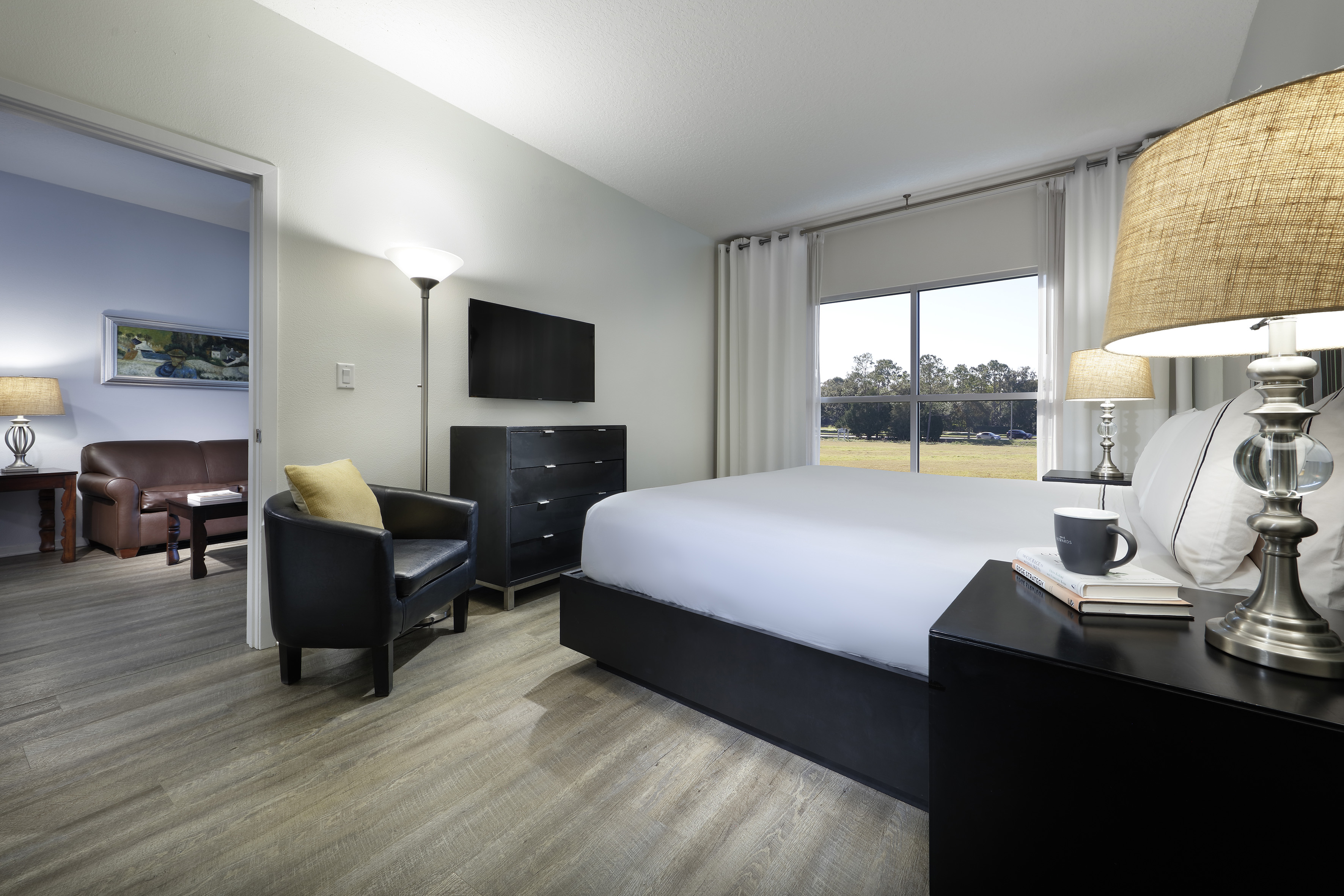 Modern hotel bedroom suite with bed, window view, TV, and living room access.
