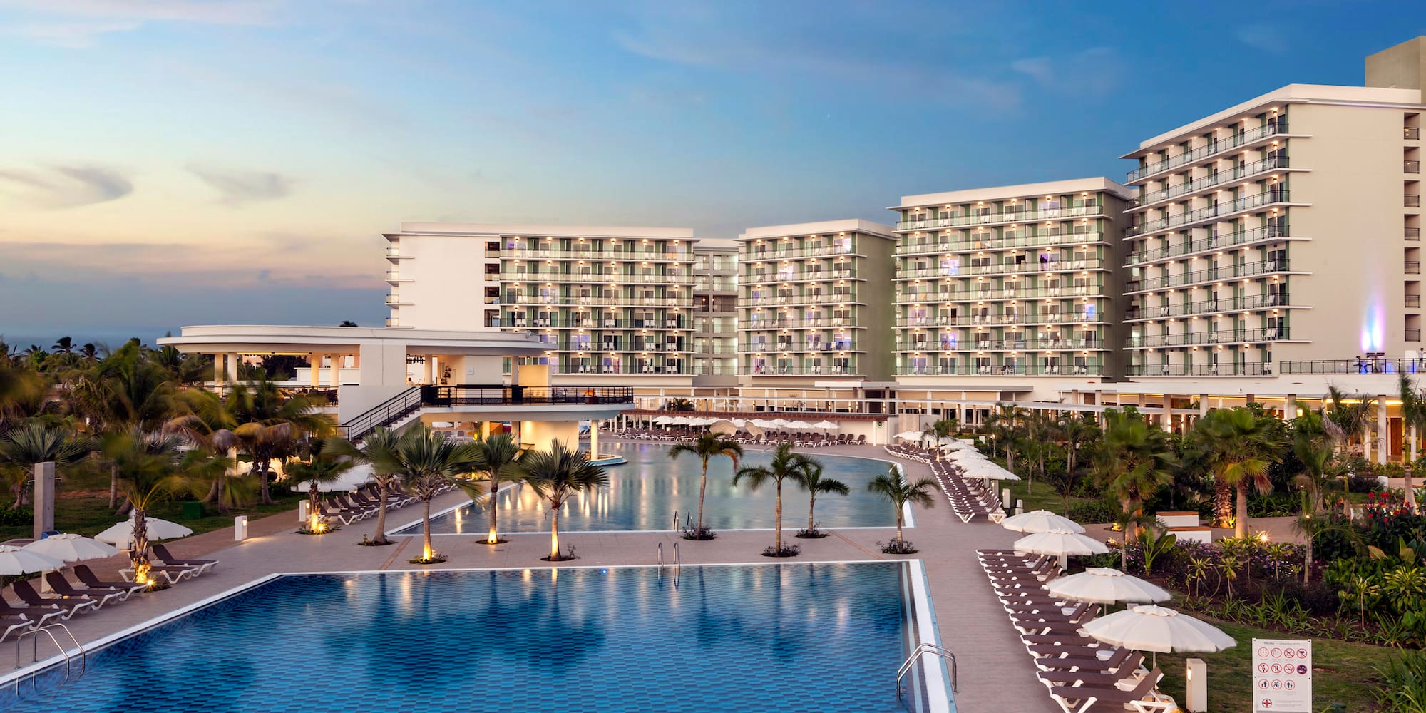 a swimming pool with palm trees and a building with a blue sky