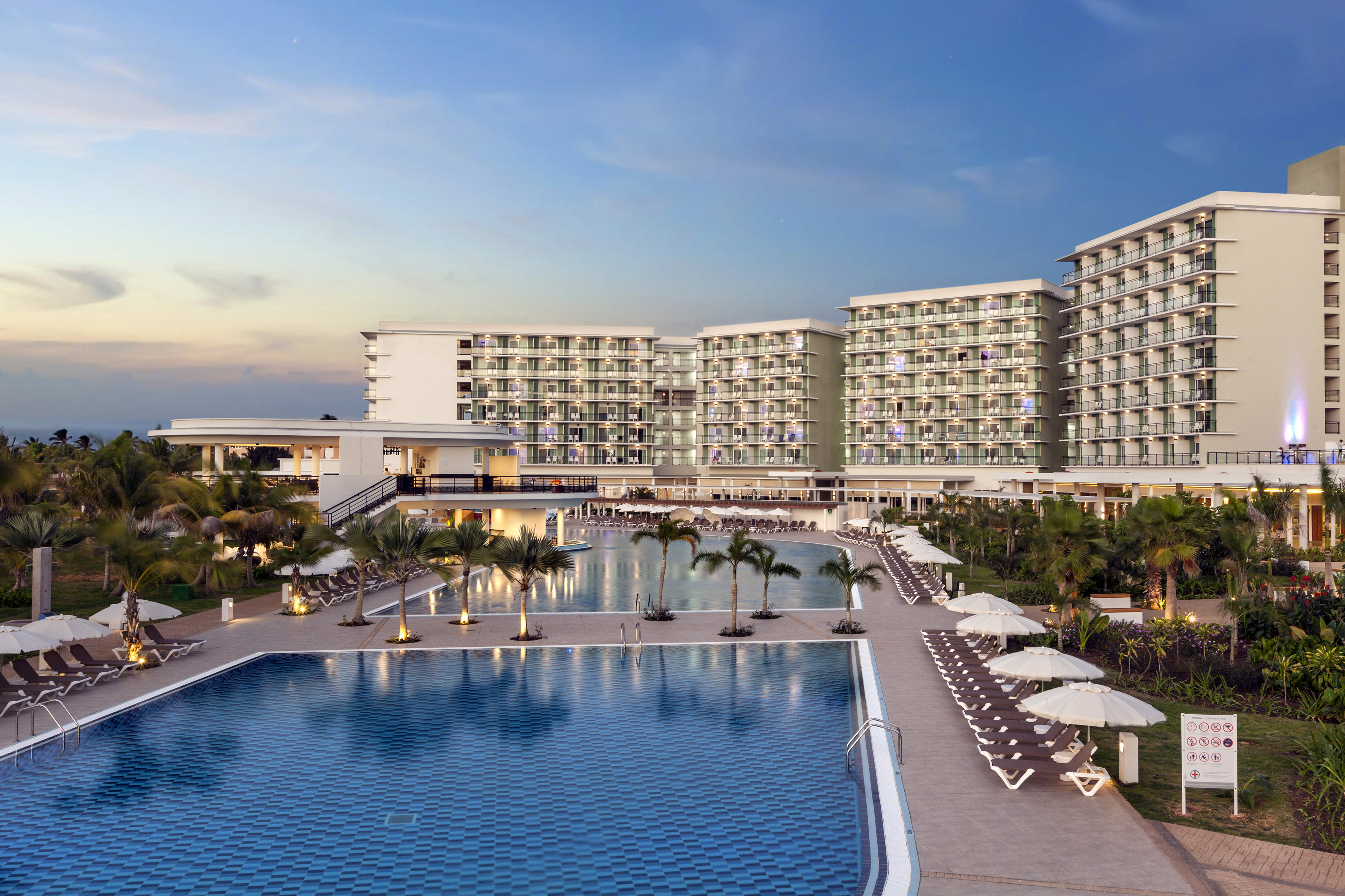 a swimming pool with palm trees and a building with a blue sky