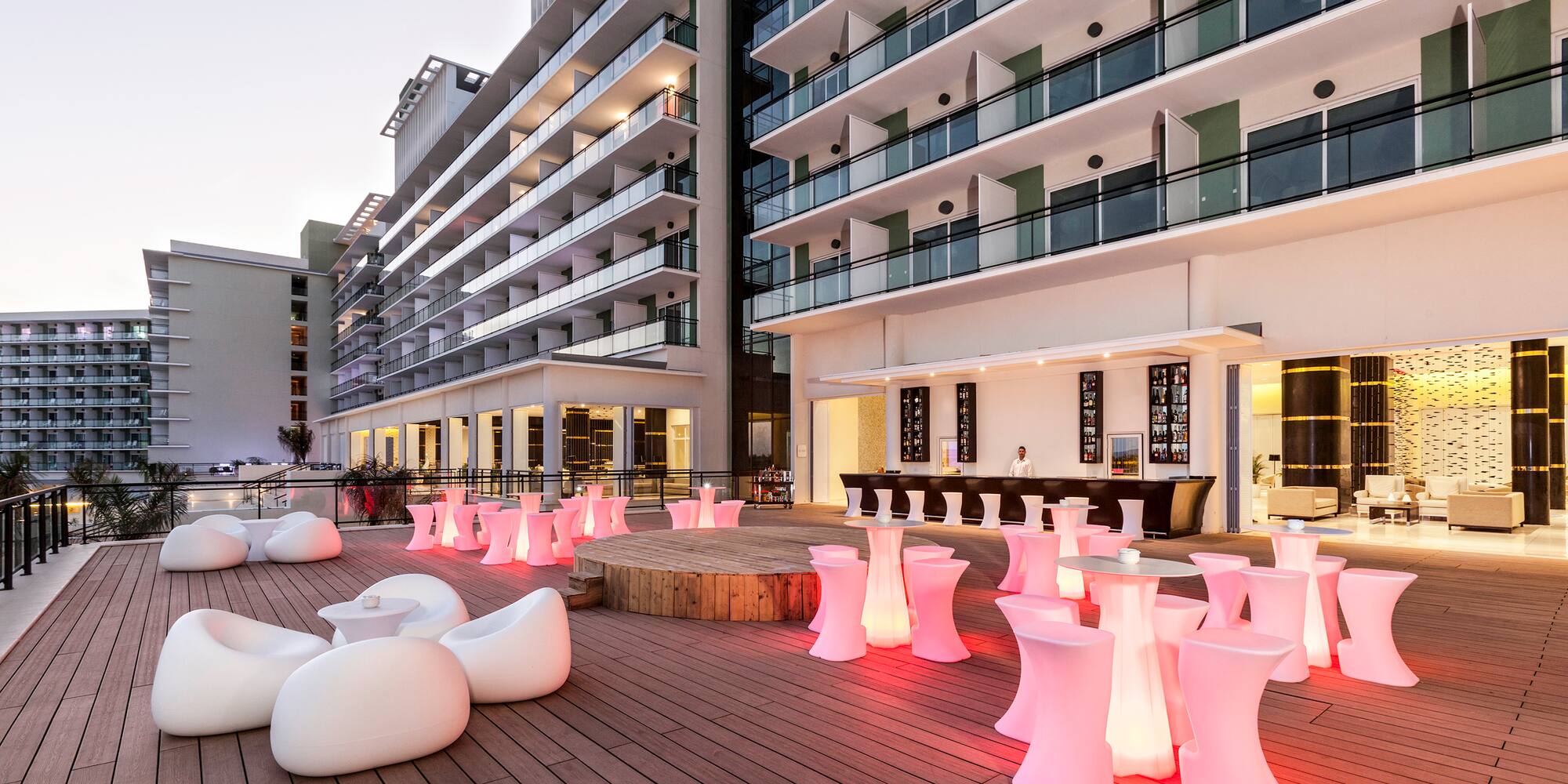 a patio with white chairs and tables with pink lights
