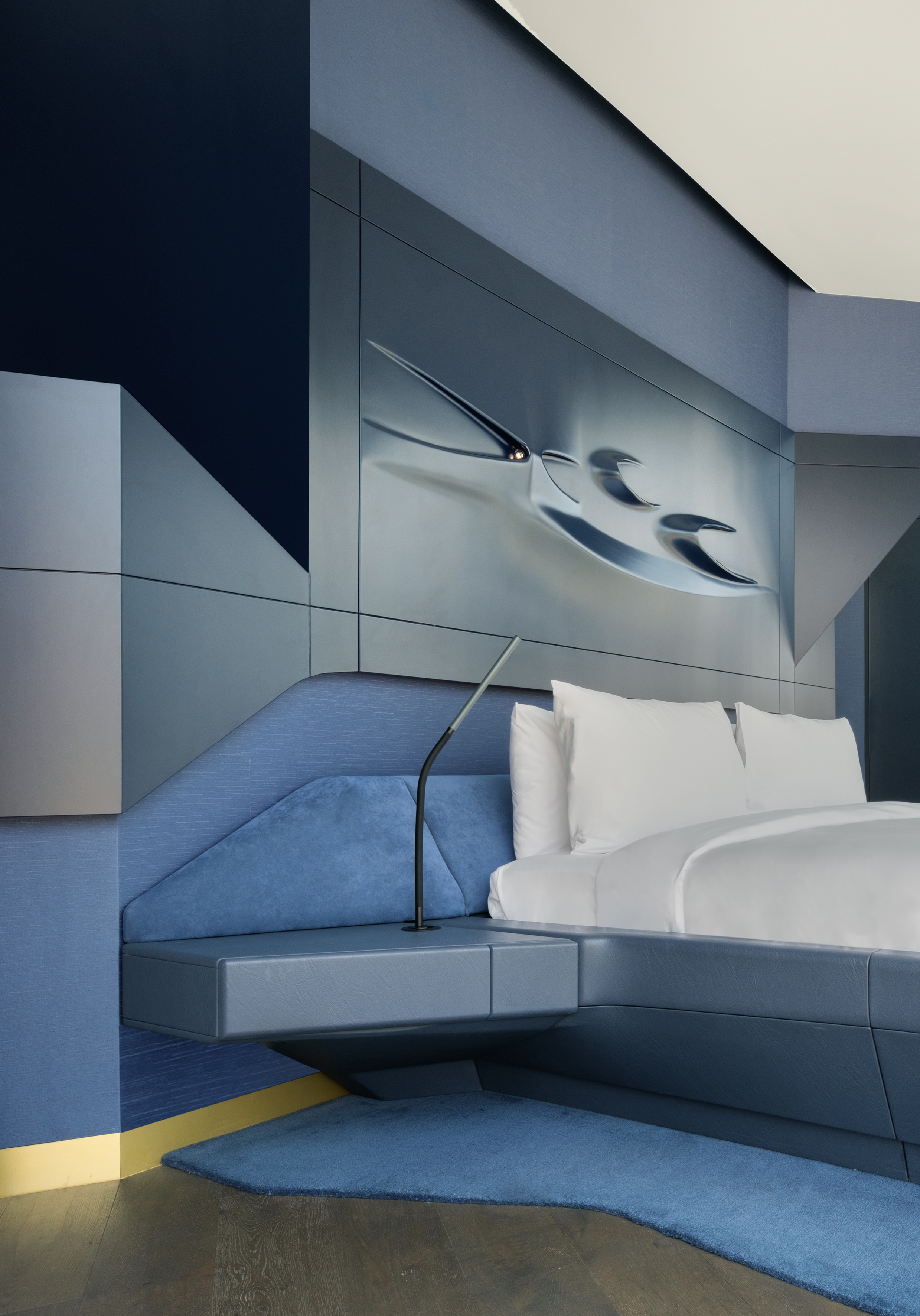 Modern blue bedroom with white bed, abstract metallic wall art, and geometric design.