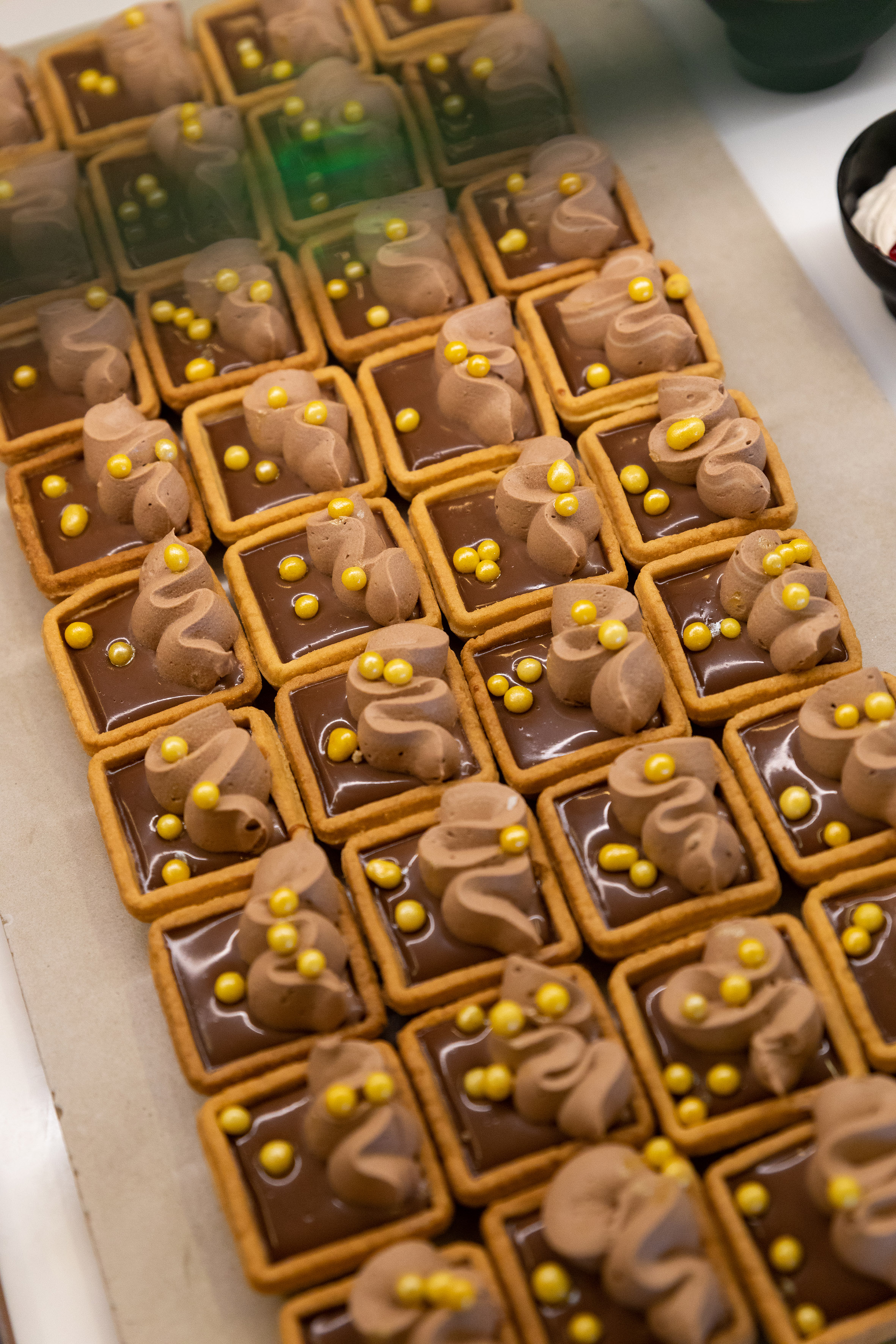 Mini chocolate tarts with cream and golden sprinkles in a display.
