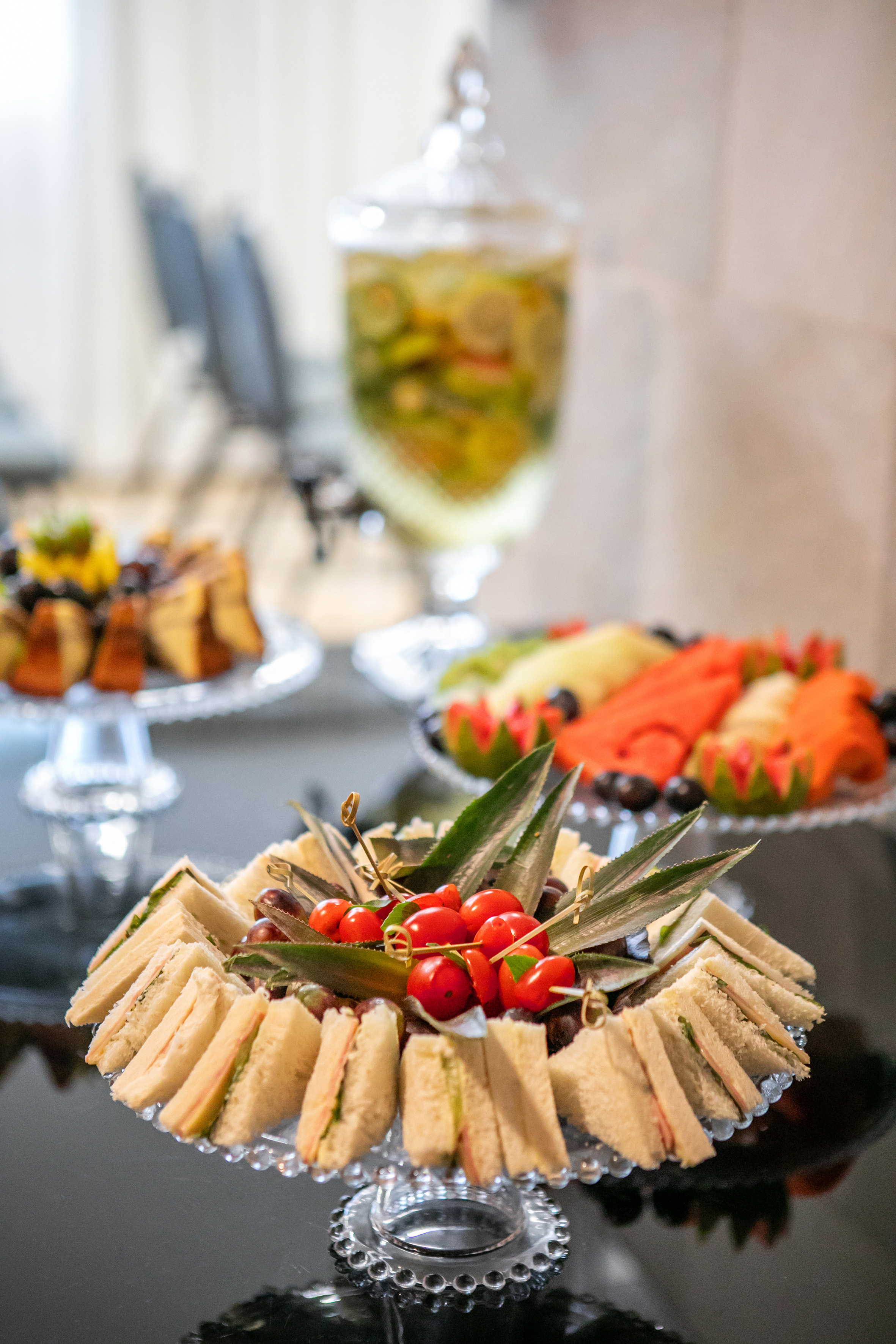 Mini sandwiches platter, fresh fruit, and drink dispenser on a party buffet.