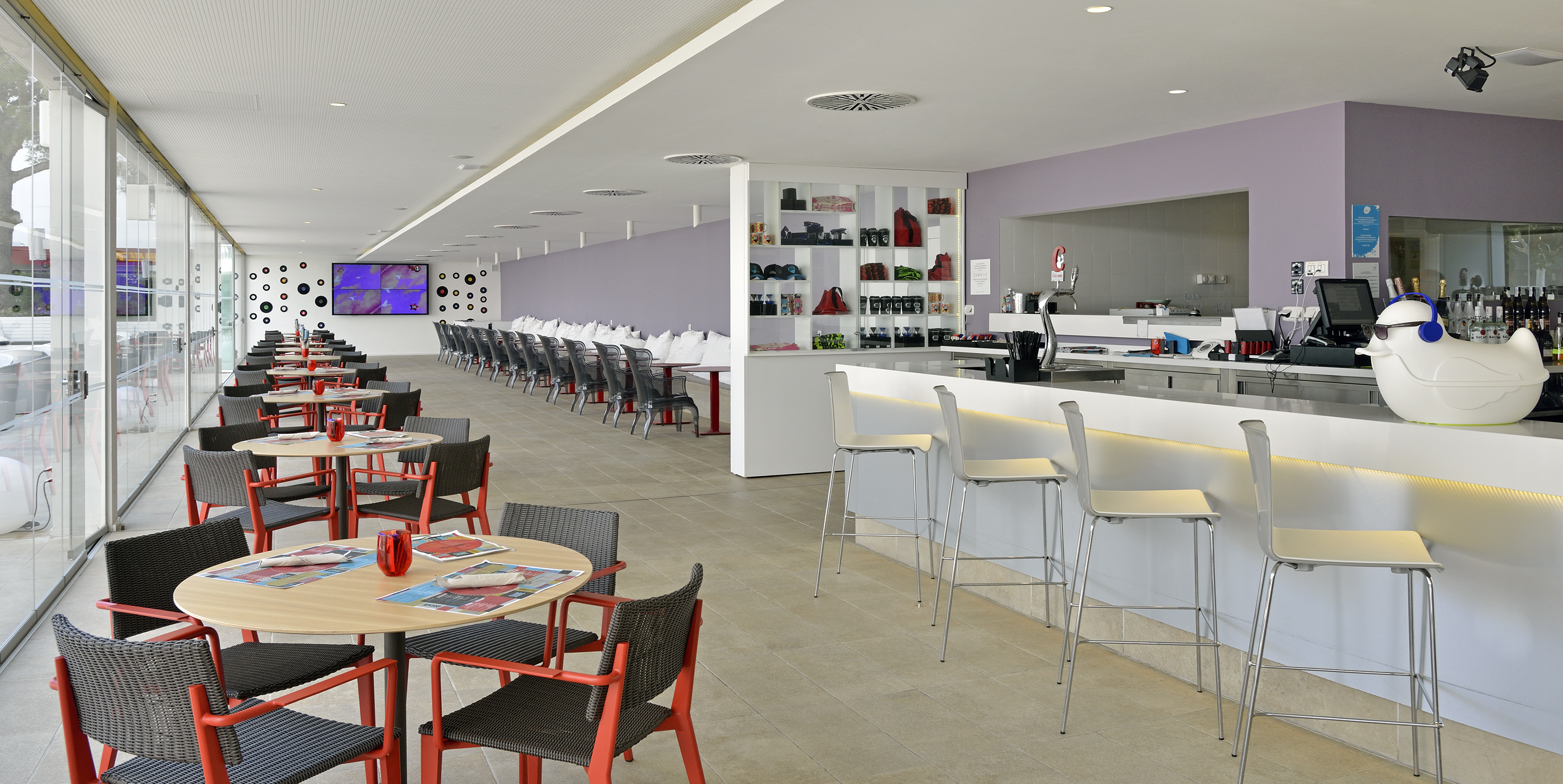 Bright modern cafe bar with dining tables, red chairs, and a white counter.