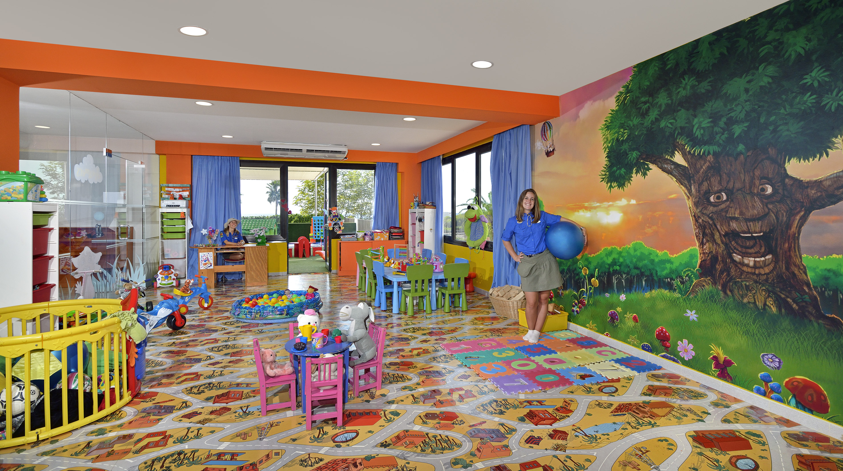 Modern nursery with three wooden cribs, star teepee, play kitchen, and grey poufs.