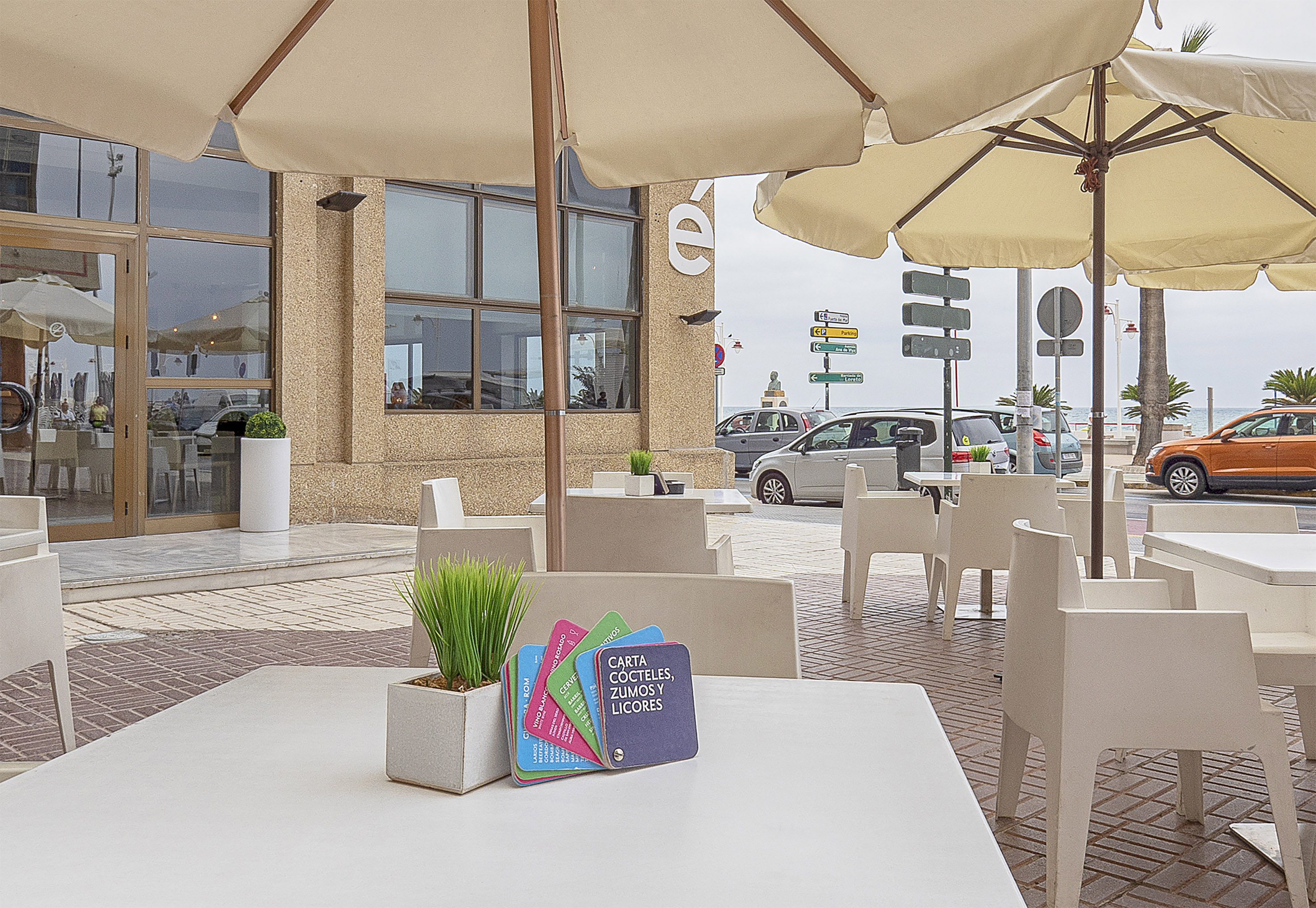 Seaside cafe terrace with umbrellas, white tables, and cocktails menu.