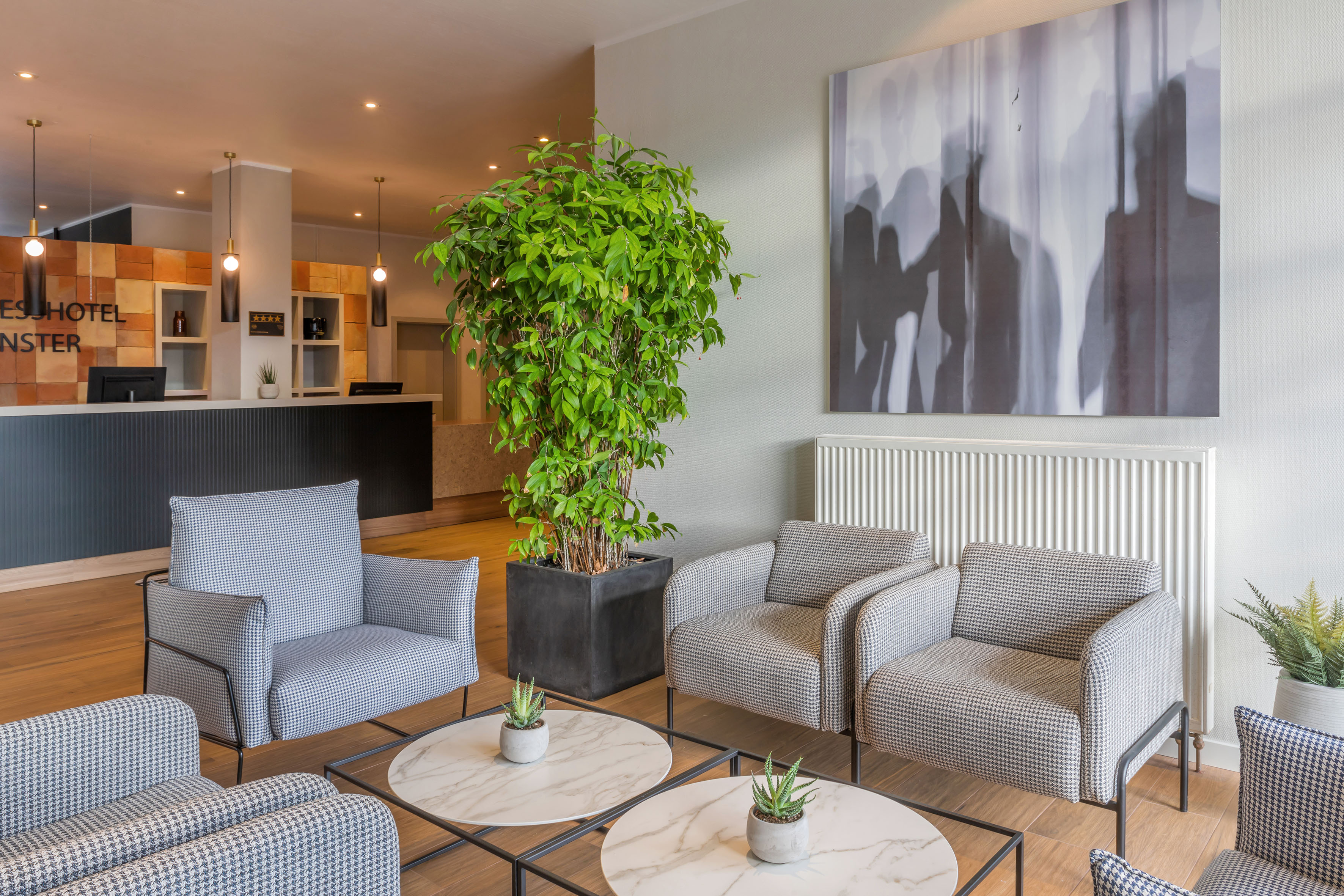 Hotel lobby with houndstooth armchairs, modern reception desk, large plant, and abstract art.