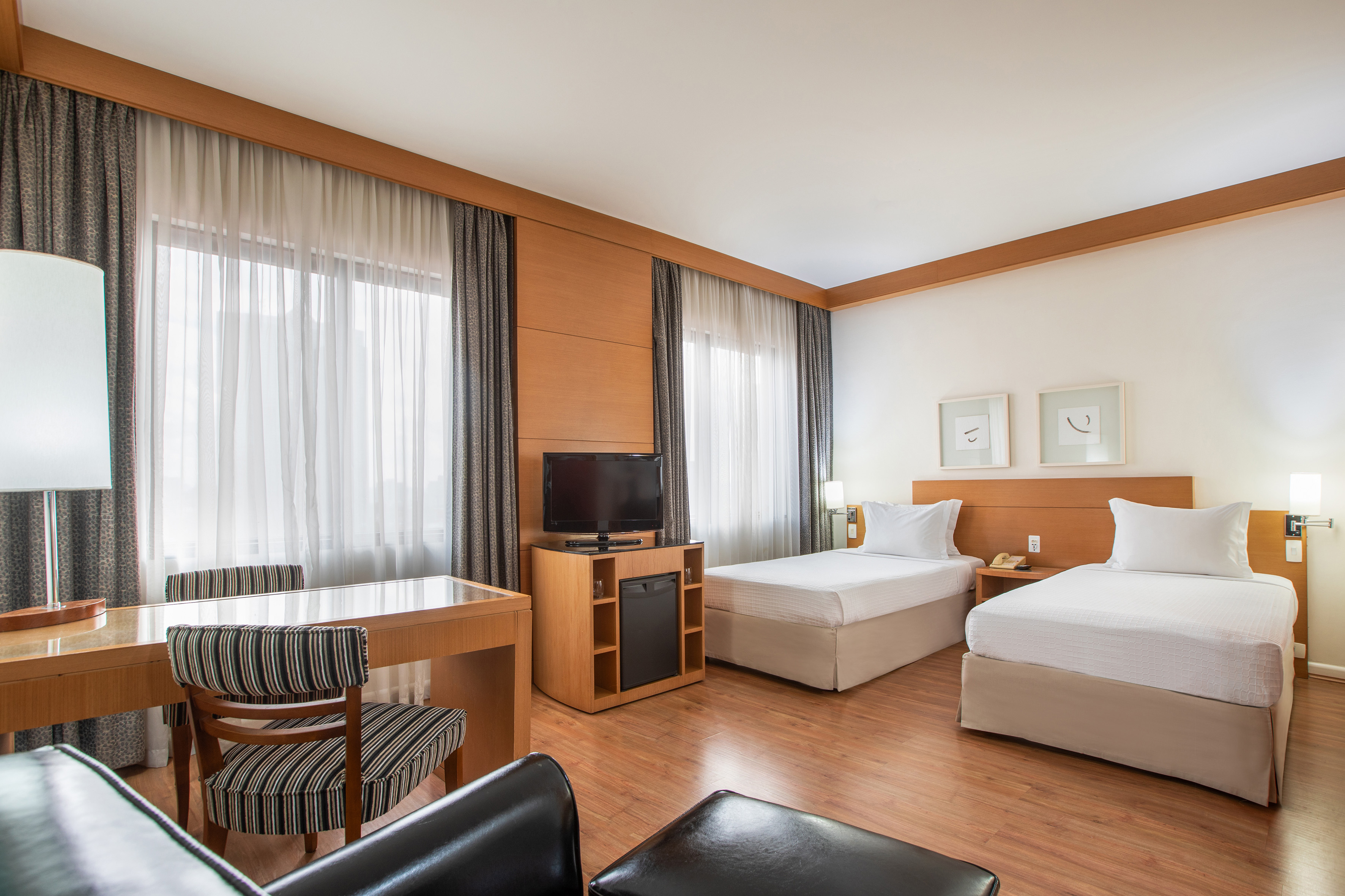 Hotel room with twin beds, a wooden desk, TV, and large windows.