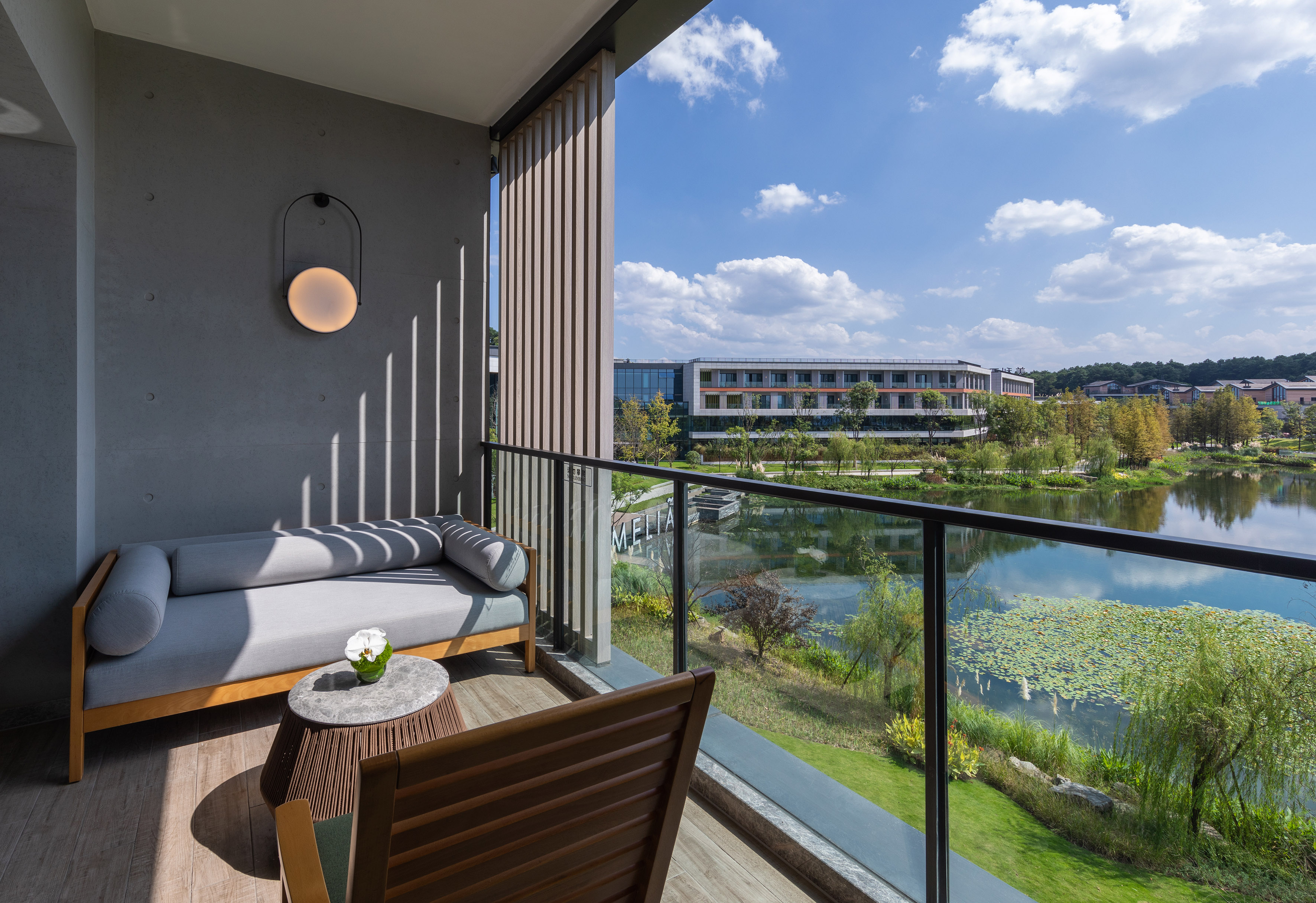 Modern hotel balcony with lake view, outdoor sofa, and resort building.