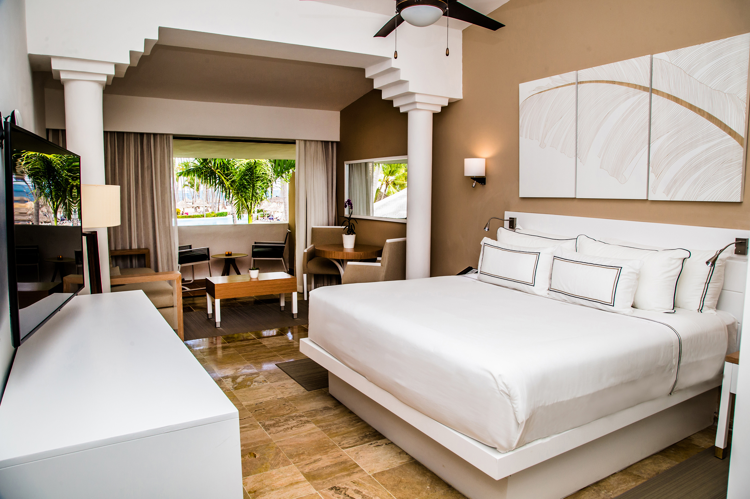 Modern hotel room with king bed, balcony, and tropical palm tree view.