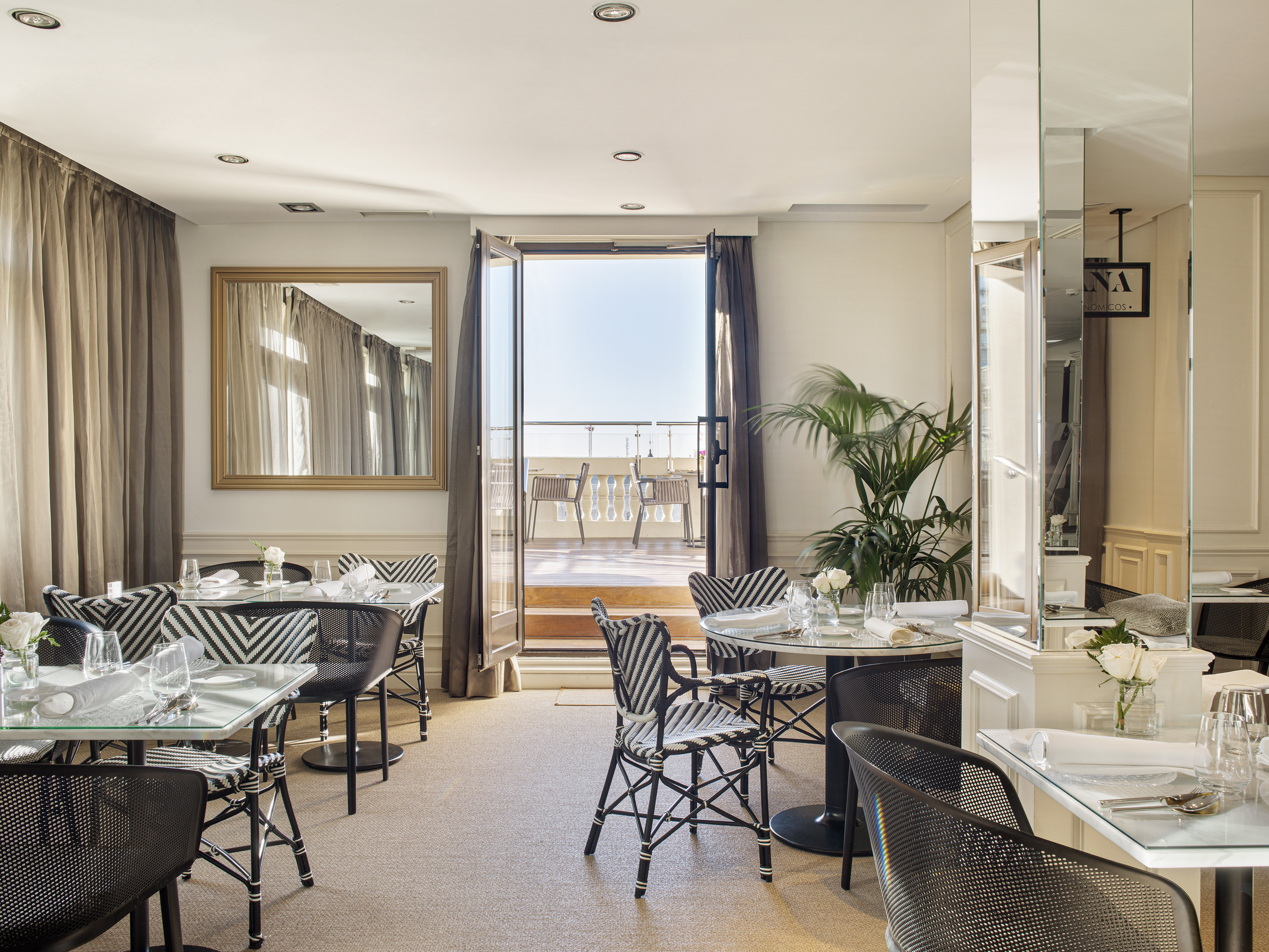 Elegant restaurant dining room with modern chairs, set tables, and bright balcony views.