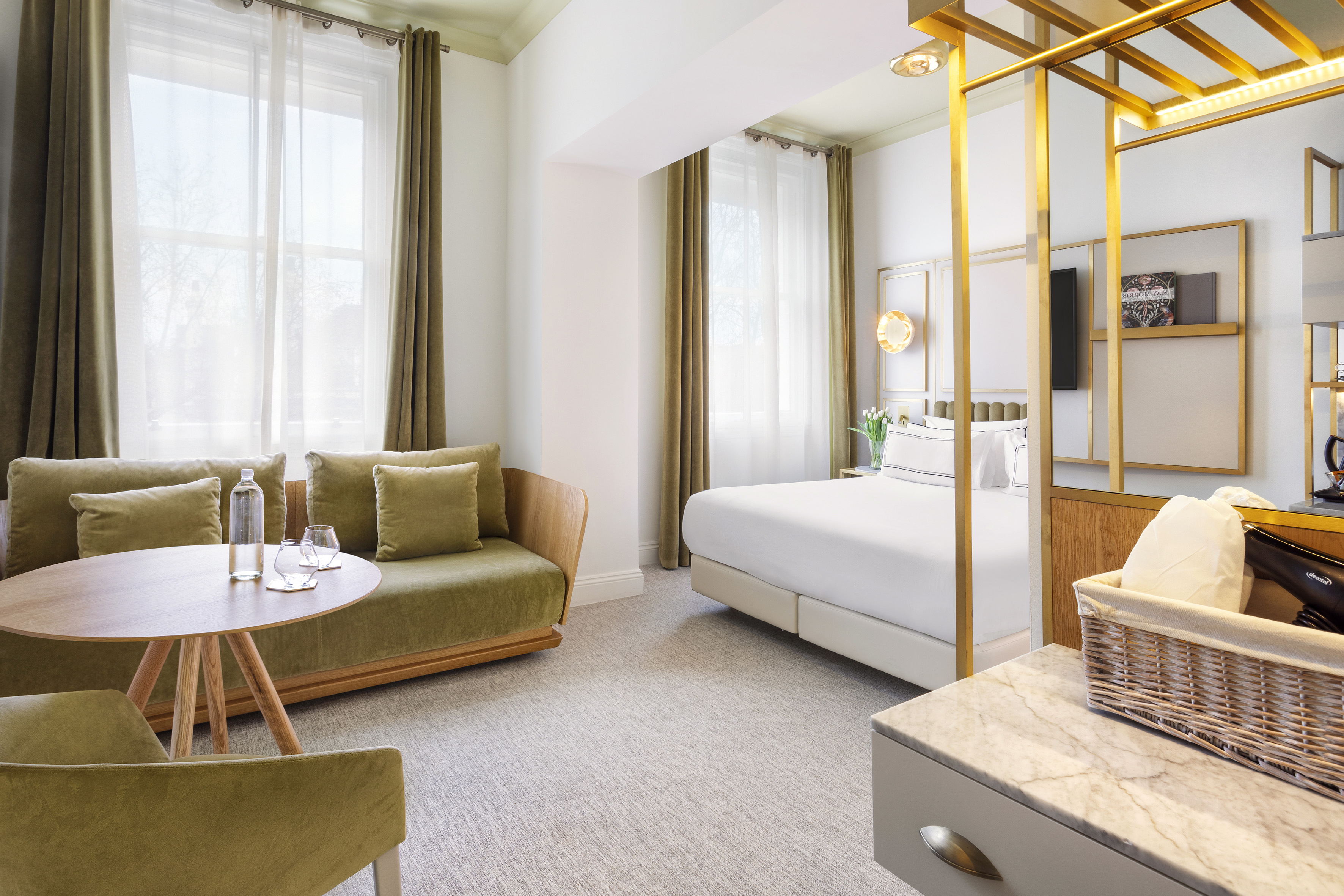 Modern hotel room with olive green sofa, golden accents, and large windows.