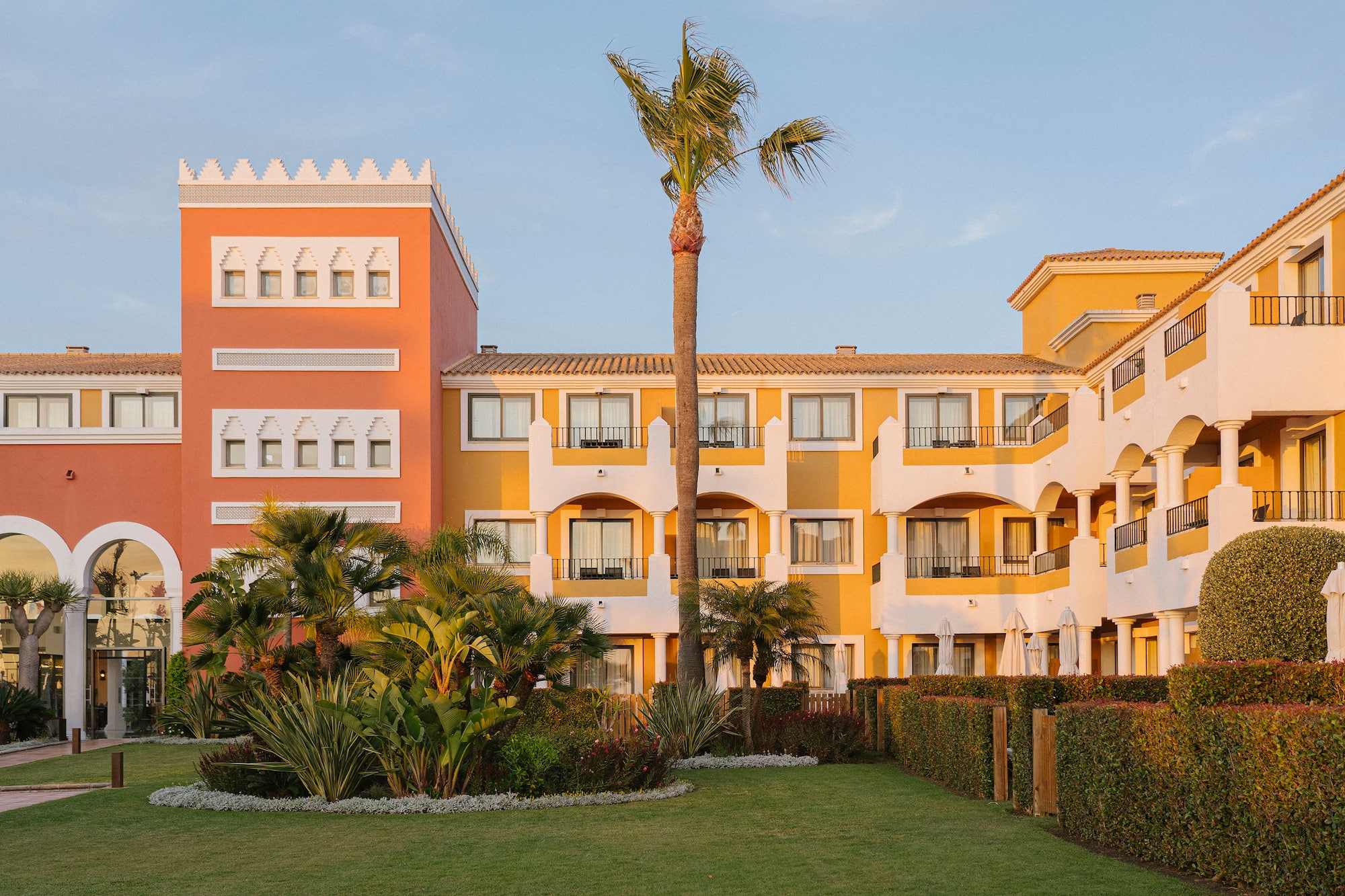 Vibrant hotel building with orange/yellow facades, palm trees, and green garden.