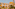 Yellow hotel with white balconies, terracotta roof, palm trees, golden hour.