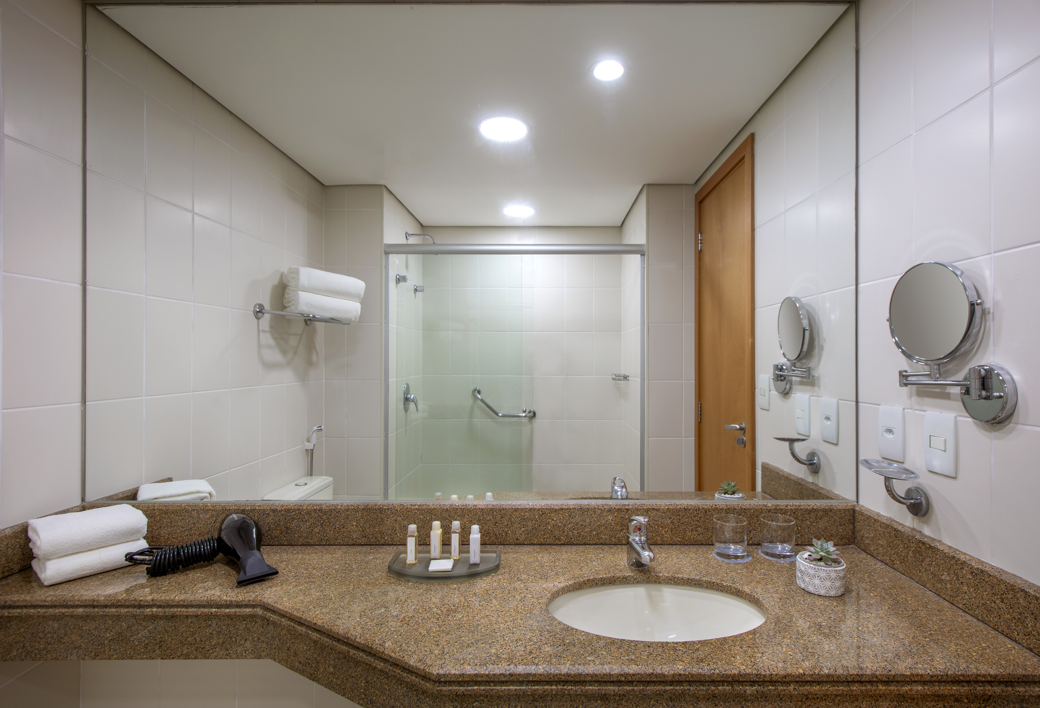 Hotel bathroom with granite vanity, large mirror, sink, and accessible shower.