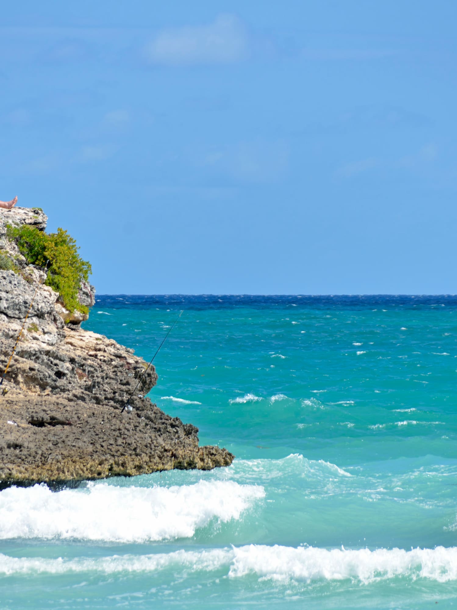 a man sitting on a rock with a fishing pole on a rocky cliff