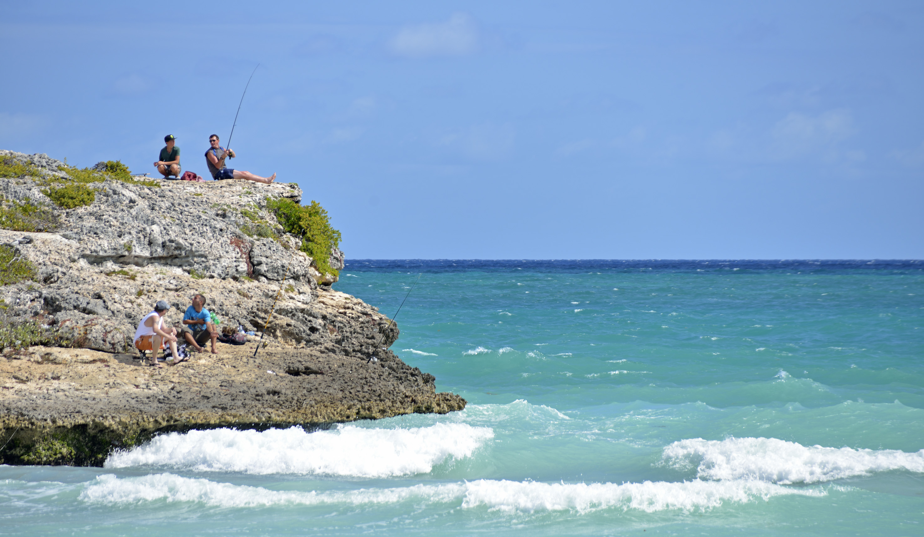 a man sitting on a rock with a fishing pole on a rocky cliff