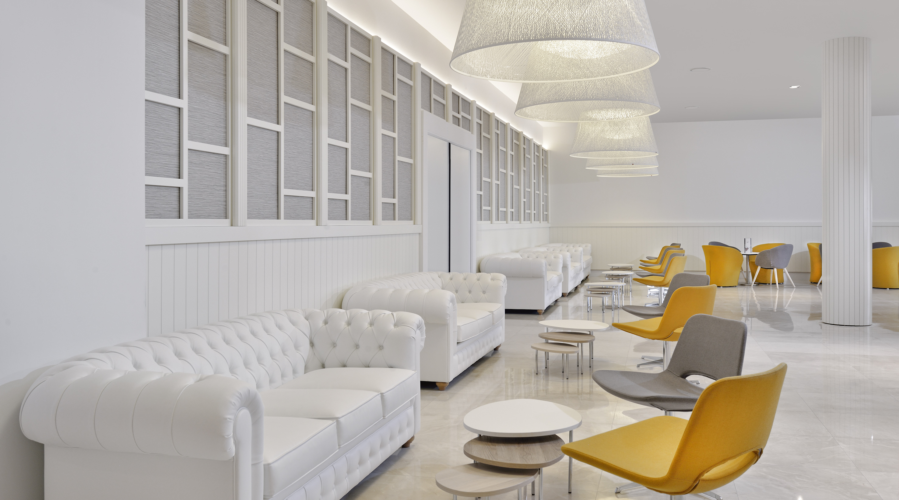 Bright hotel lobby with white tufted sofas and modern yellow, grey chairs.