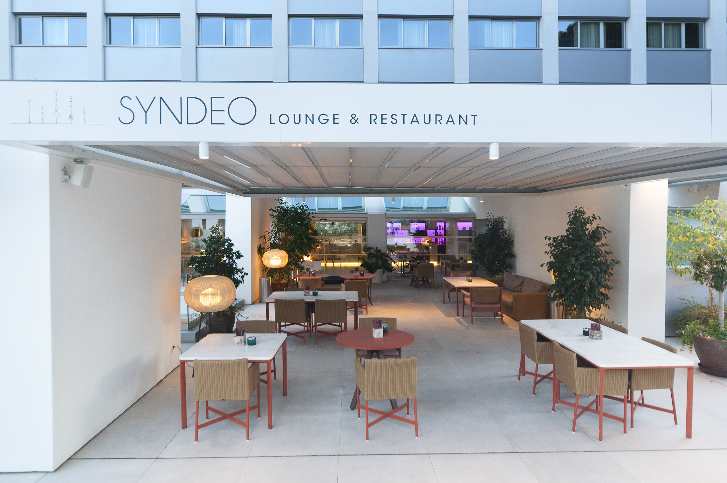 Syndeo Lounge & Restaurant outdoor patio with modern tables, chairs, and illuminated bar.