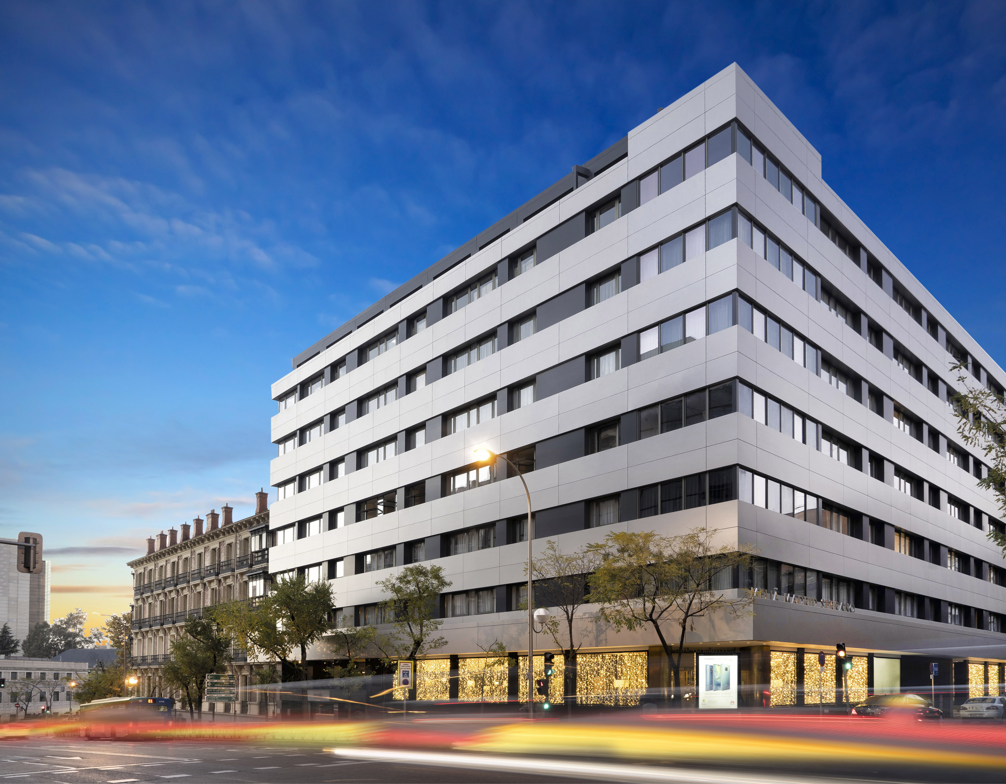 Modern white building exterior, city street at night with car light trails.