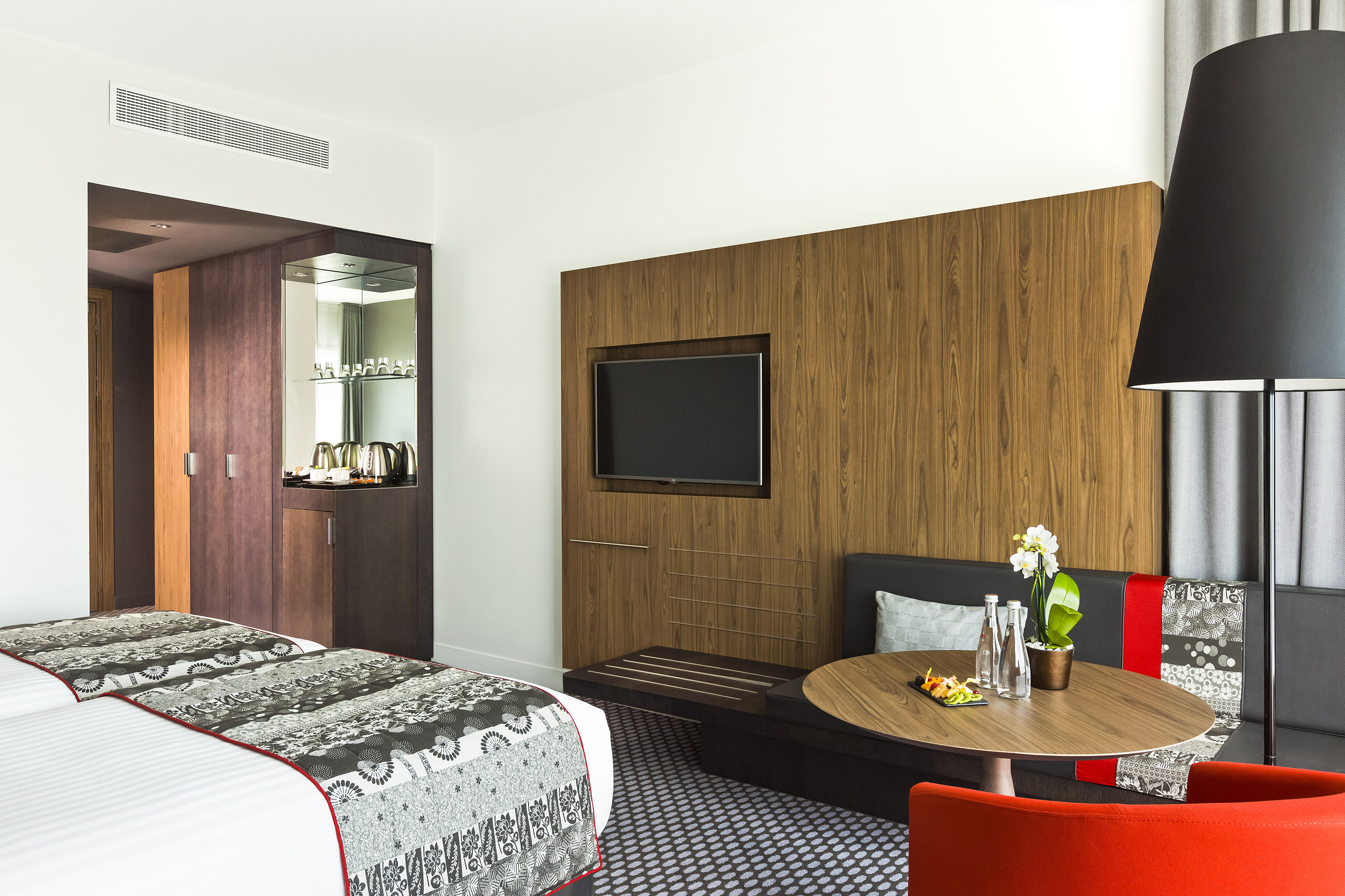 Contemporary hotel room featuring twin beds, TV, seating, and coffee station.