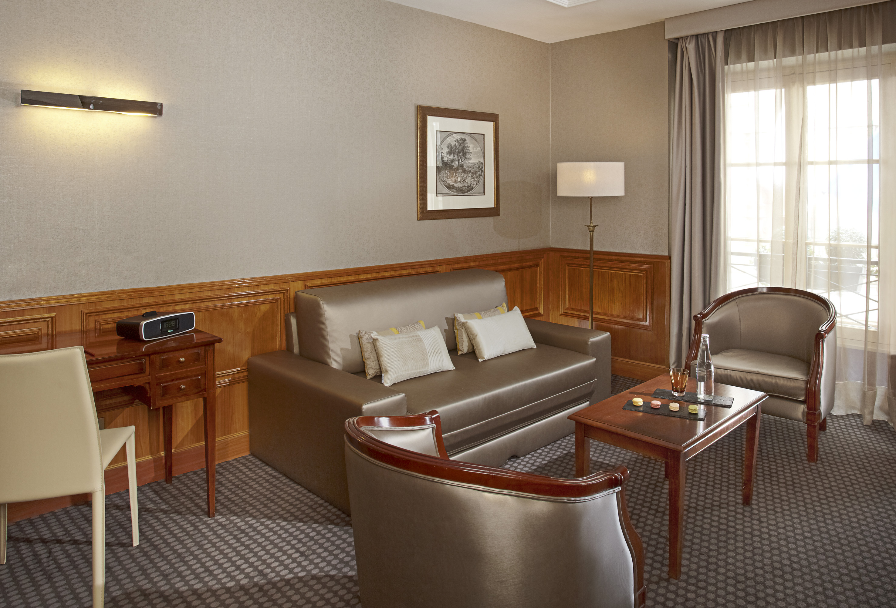 Luxury hotel suite living room with sofa bed, armchairs, and wood paneling.