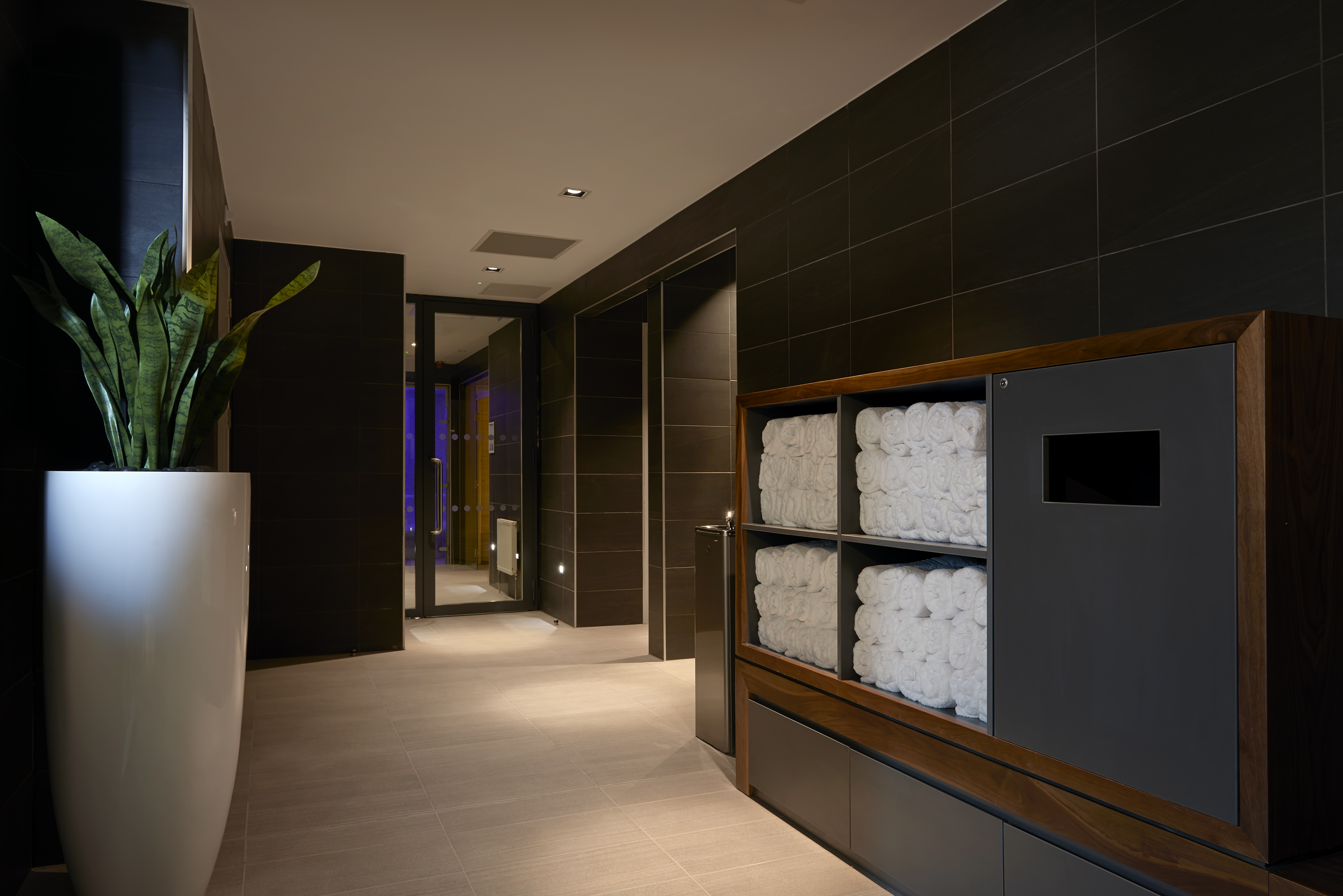Spa changing room with stacked white towels, dark tiles, and modern plant.