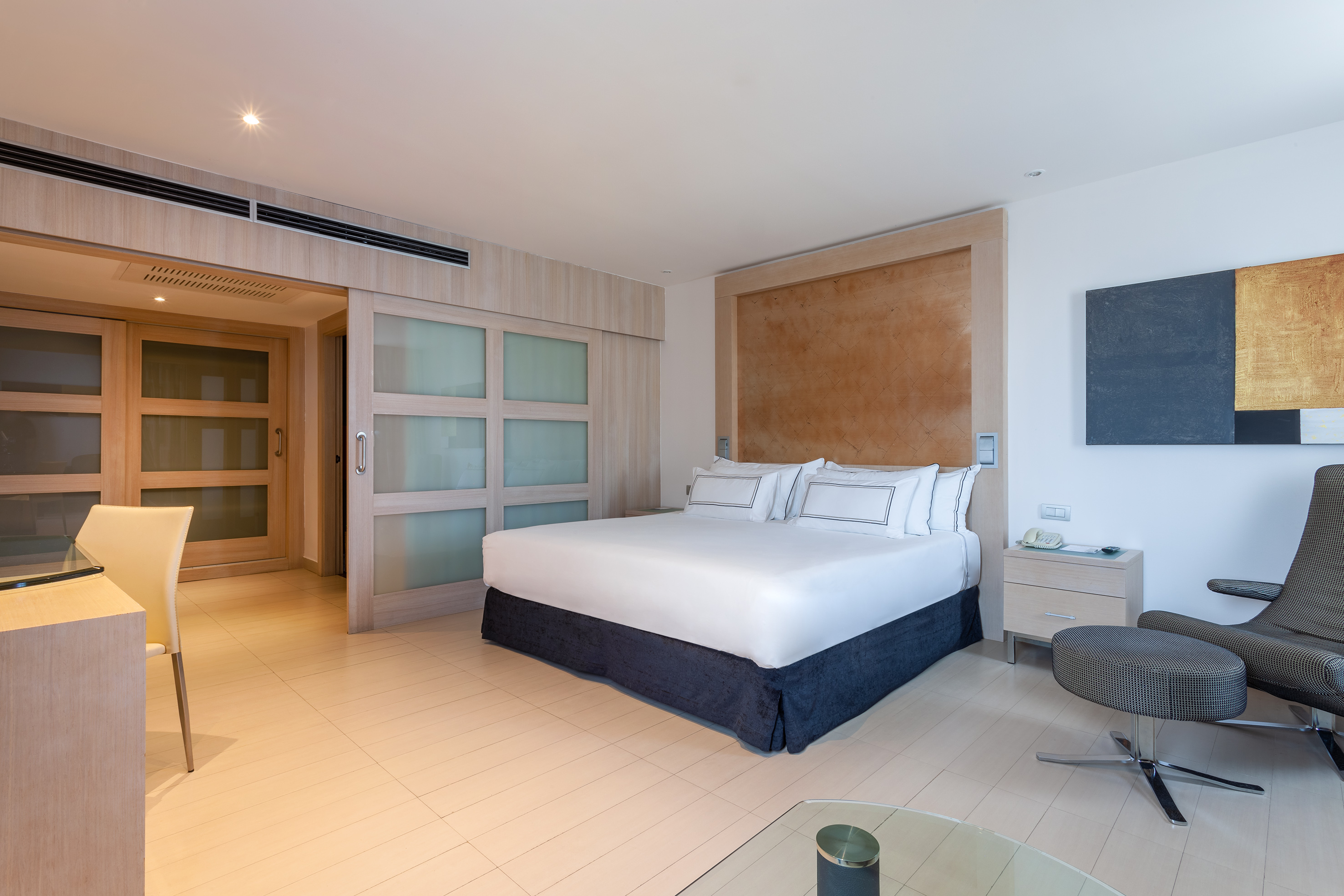 Luxury hotel room with king bed, modern decor, wood accents, and frosted sliding doors.