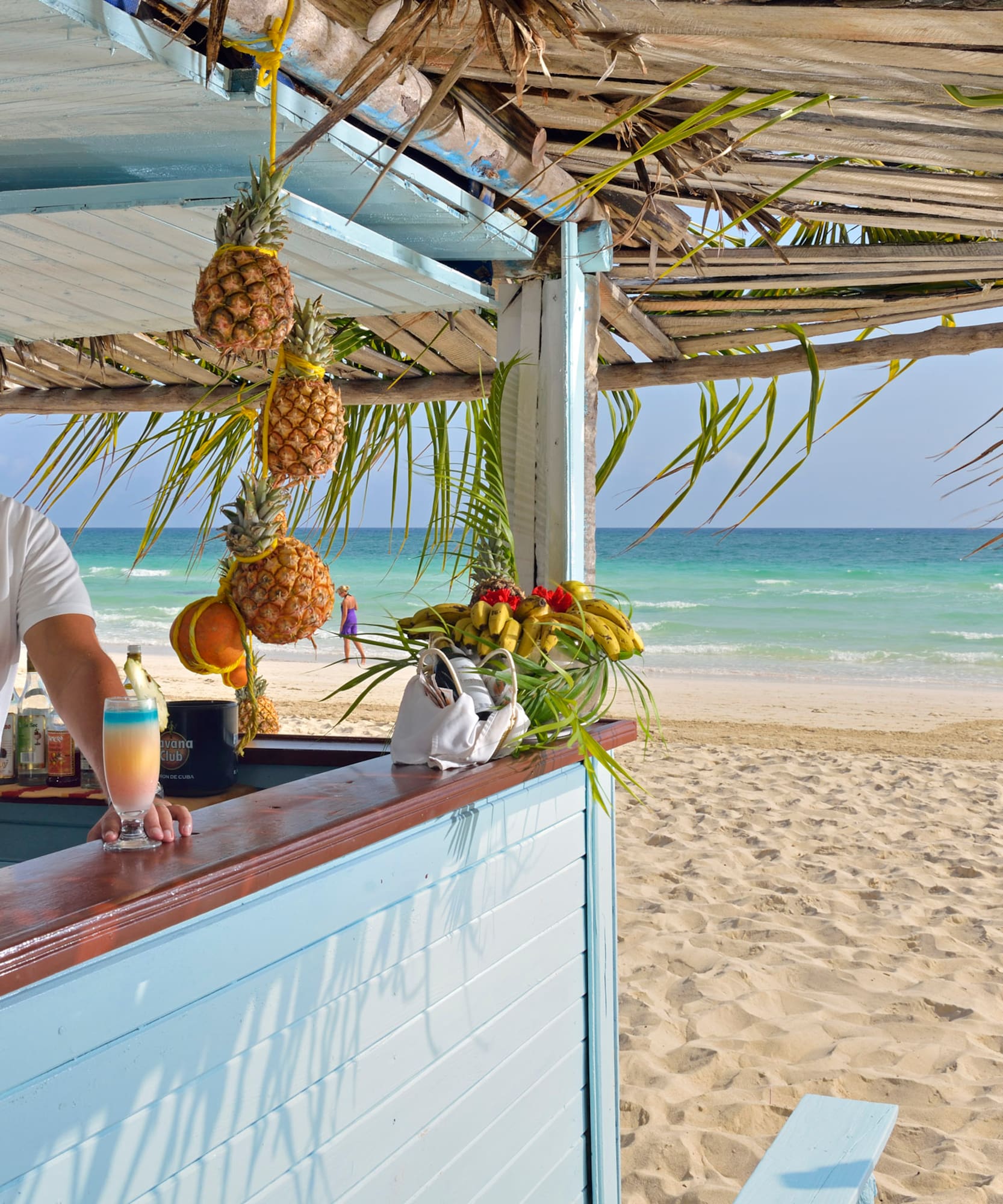 a man standing at a bar with a drink and pineapples on the beach