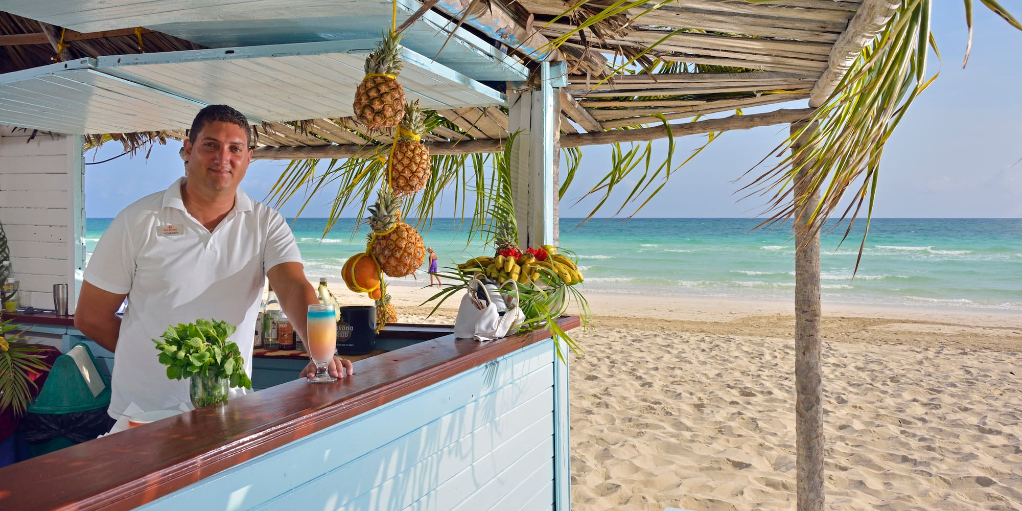 a man standing at a bar with a drink and pineapples on the beach