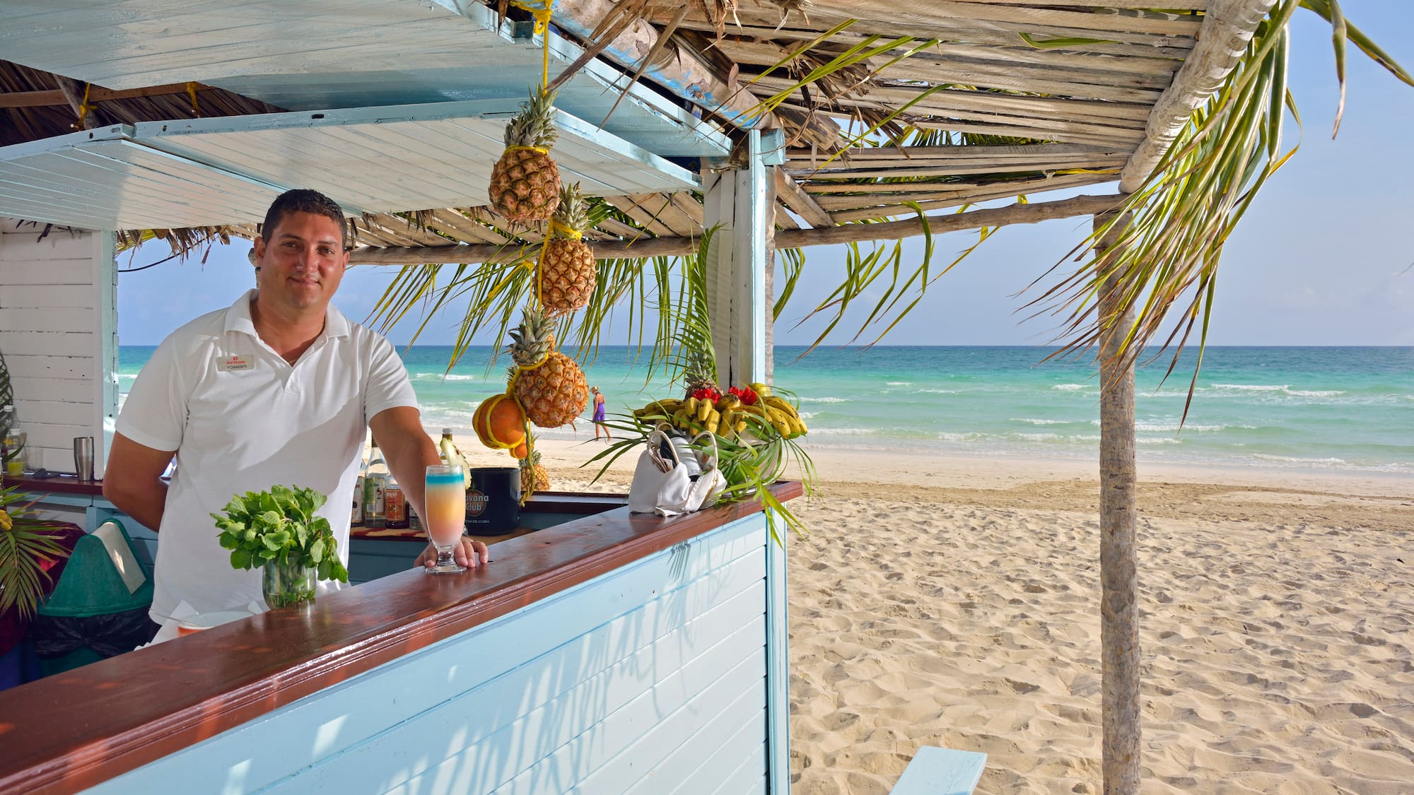 a man standing at a bar with a drink and pineapples on the beach