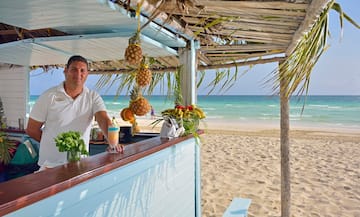 a man standing at a bar with a drink and pineapples on the beach