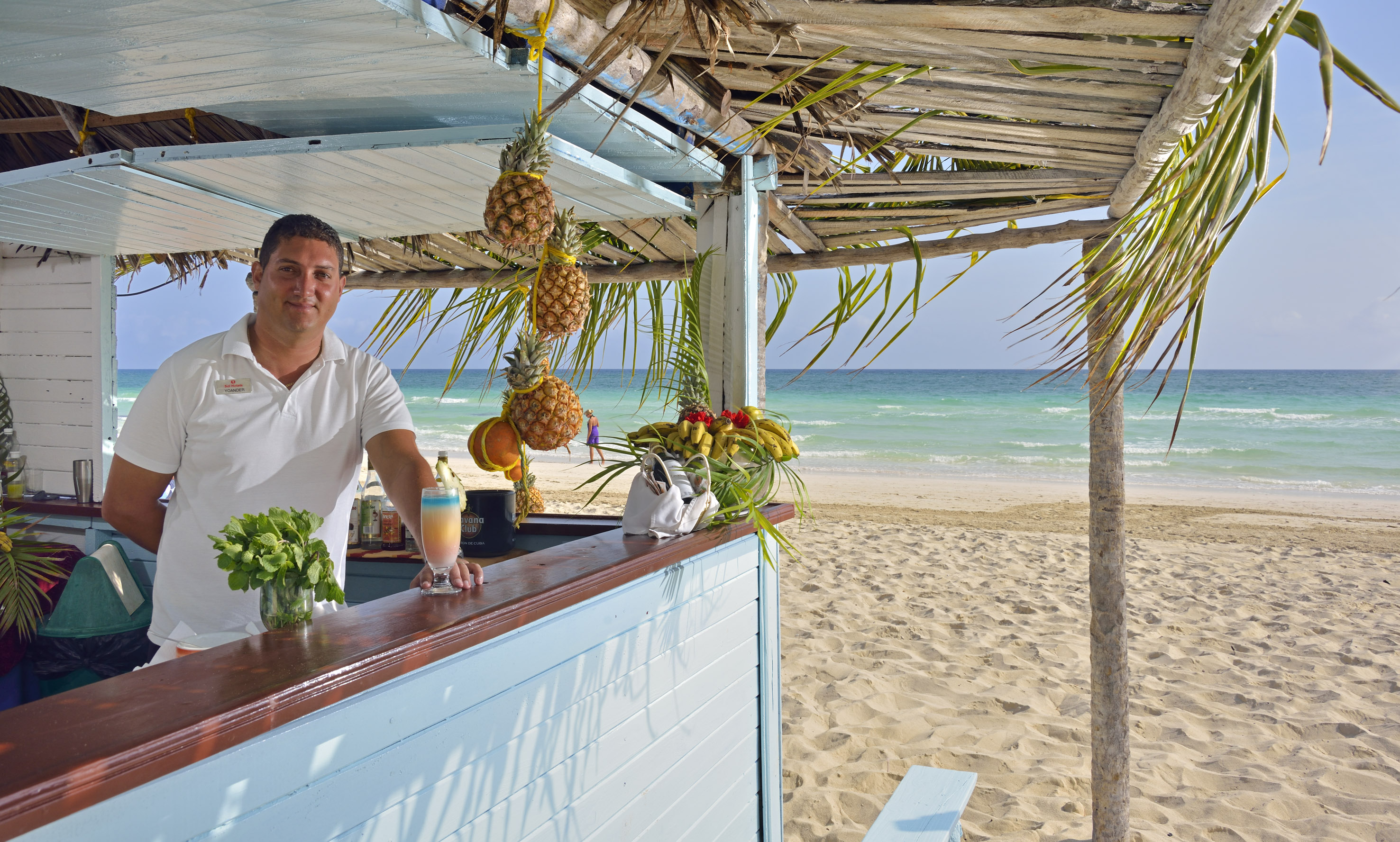 a man standing at a bar with a drink and pineapples on the beach