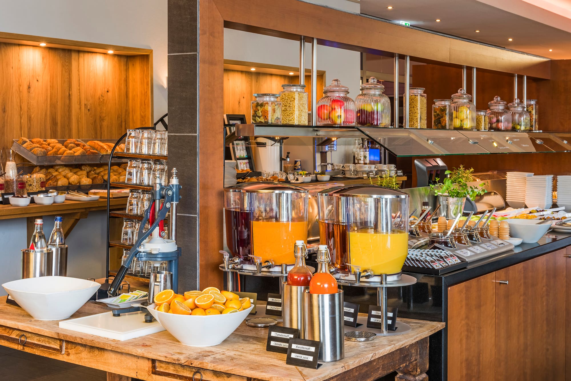 Hotel breakfast buffet with fresh orange juice, baked goods, and cereal jars.