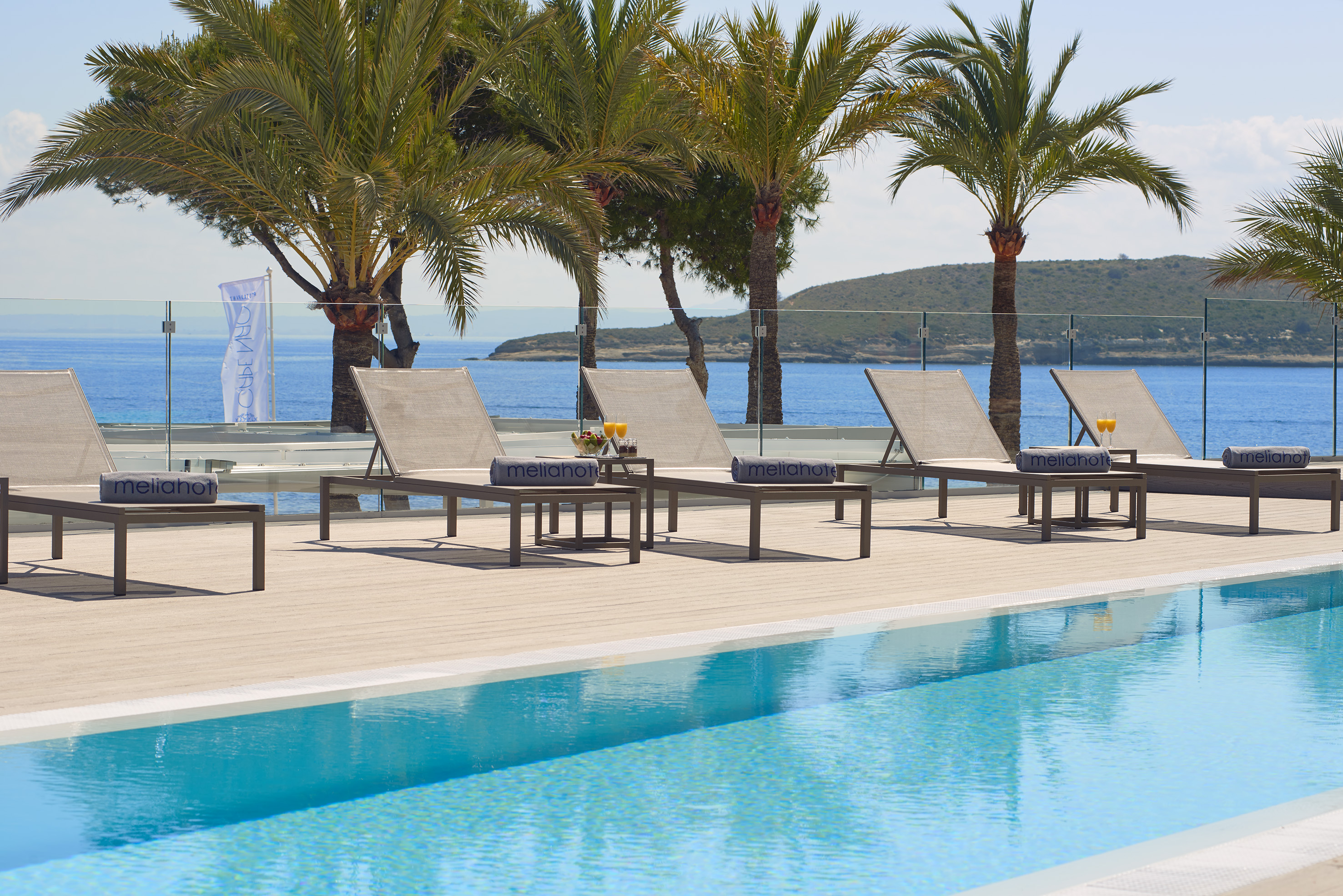 Meliá hotel pool deck with ocean view, sun loungers, palm trees, and drinks.