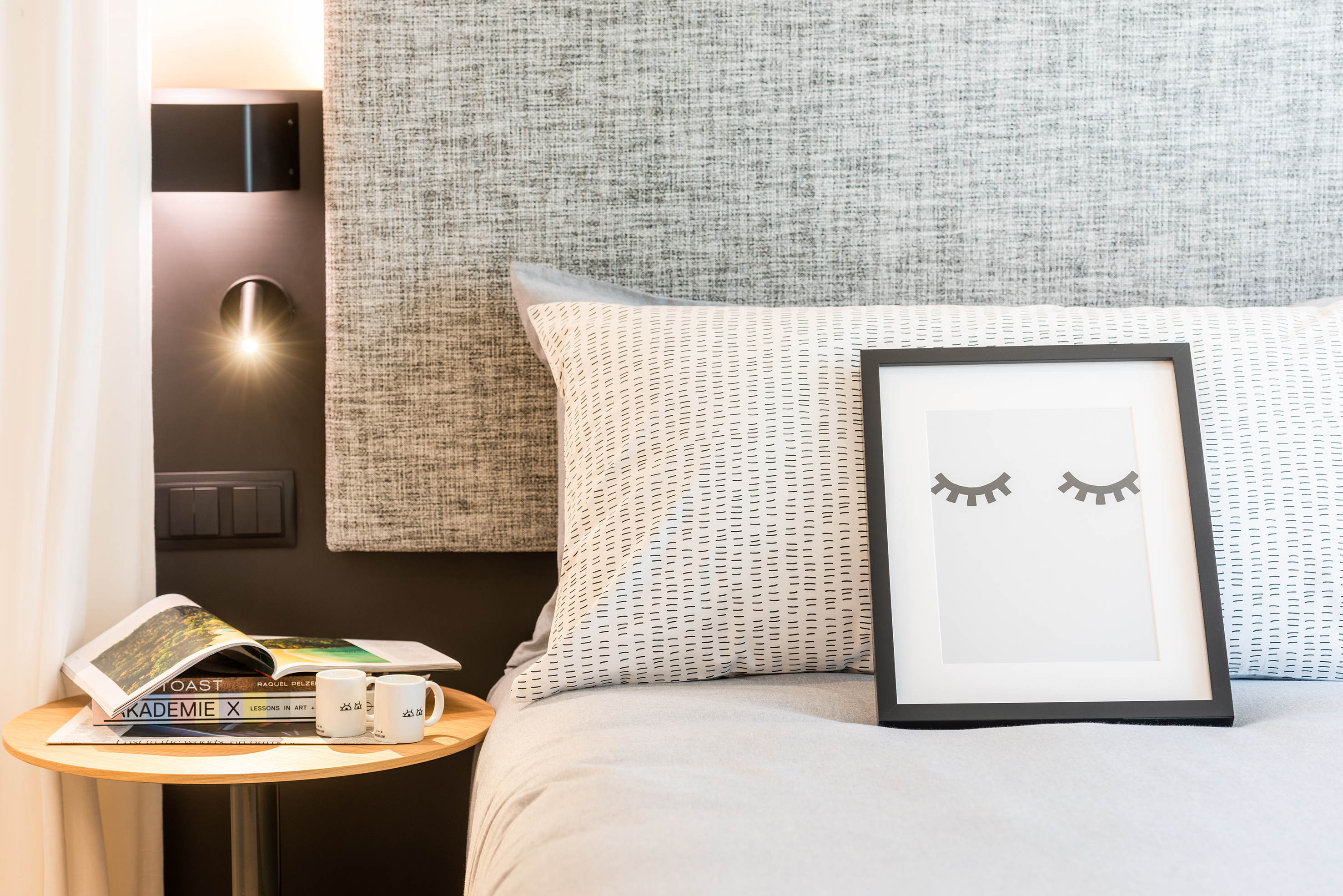 Modern bedroom with patterned pillow, framed eyelash art, and lit bedside.